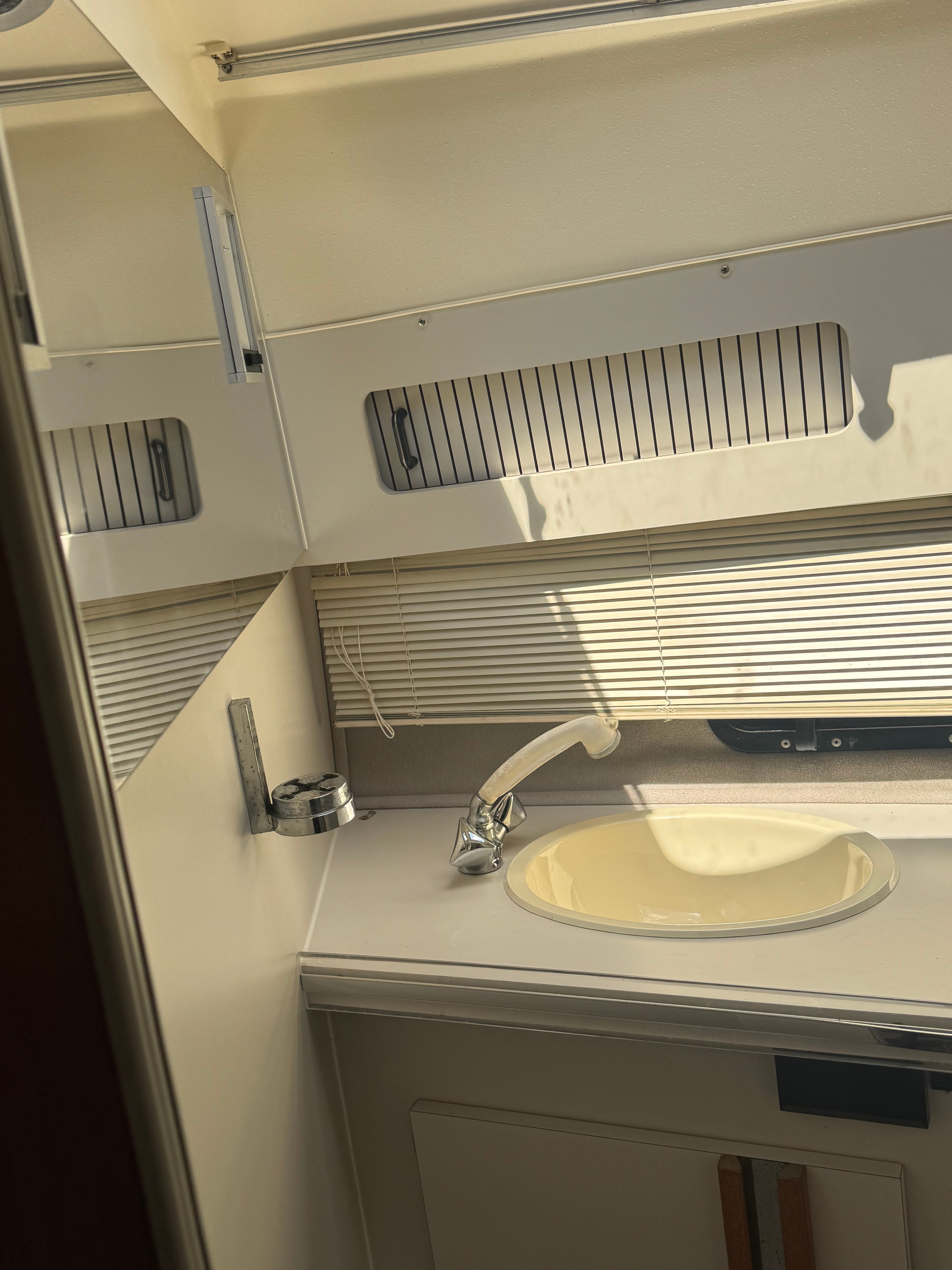 Interior view of a boat bathroom with sink, faucet, and shutters.