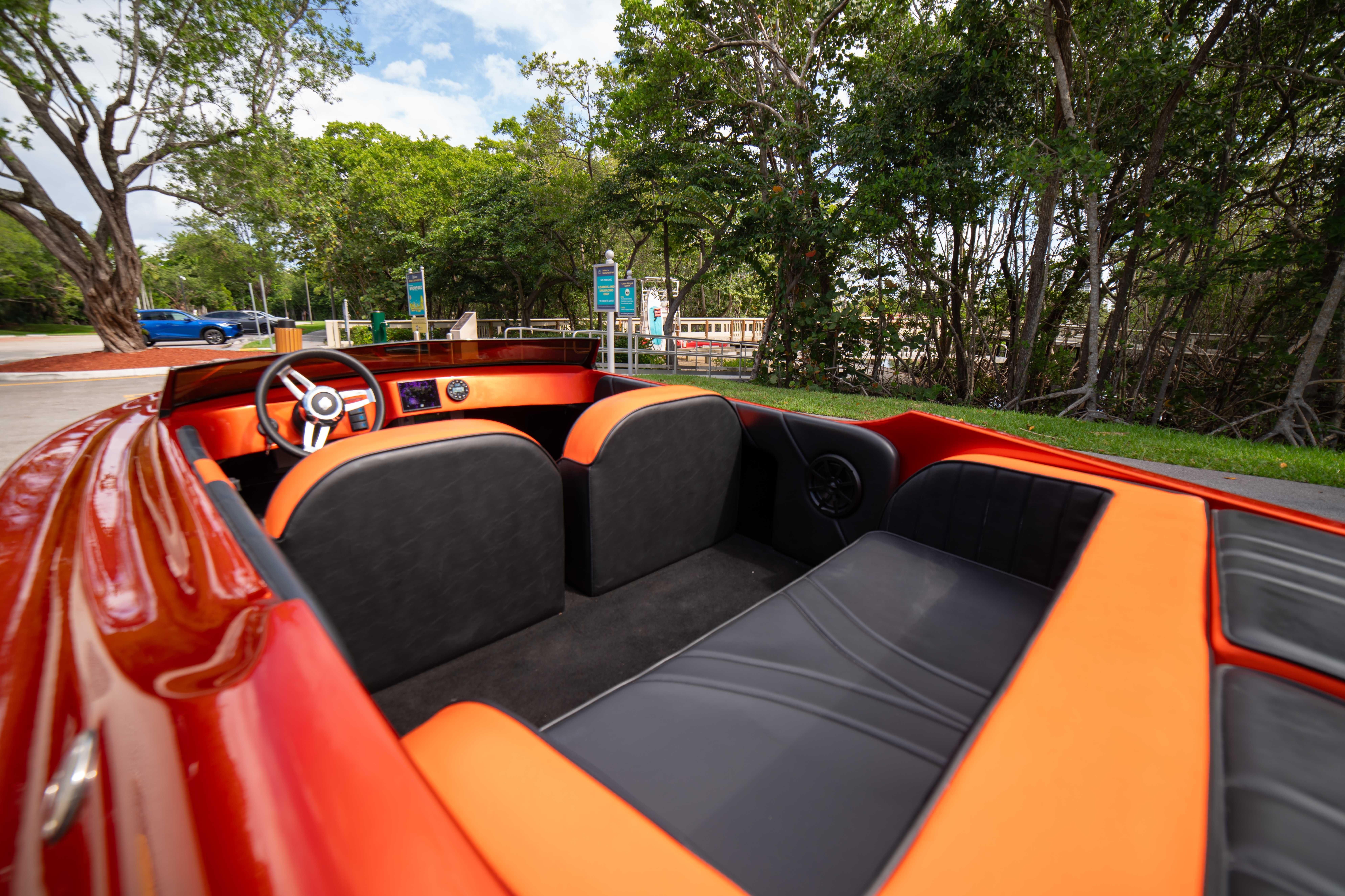 1984 Sleekcraft Aristocrat 20 boat interior with orange and black seating, parked near trees.