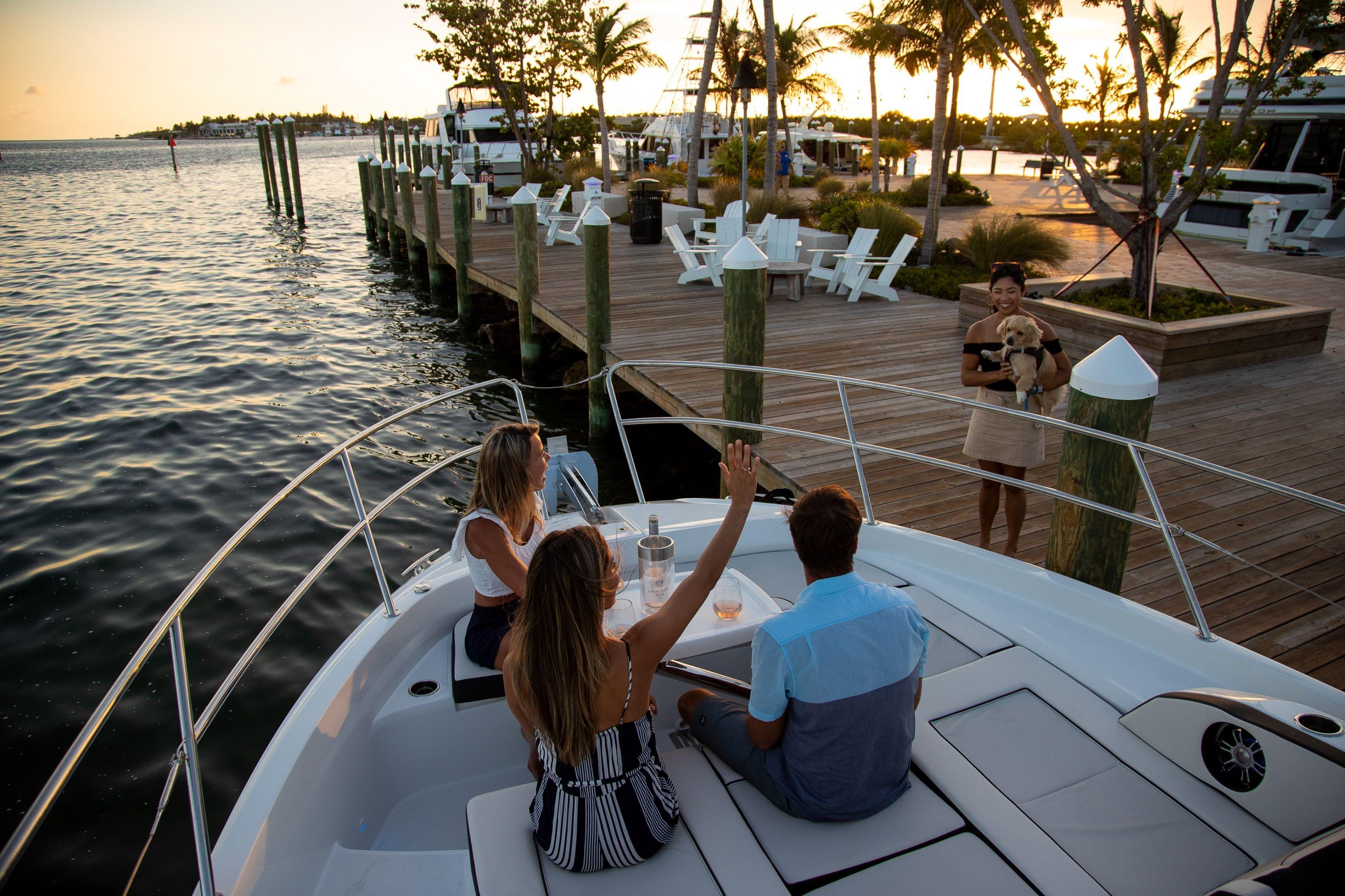 People relaxing on a 2026 Jeanneau Leader 12.5 WA boat at sunset near a dock.