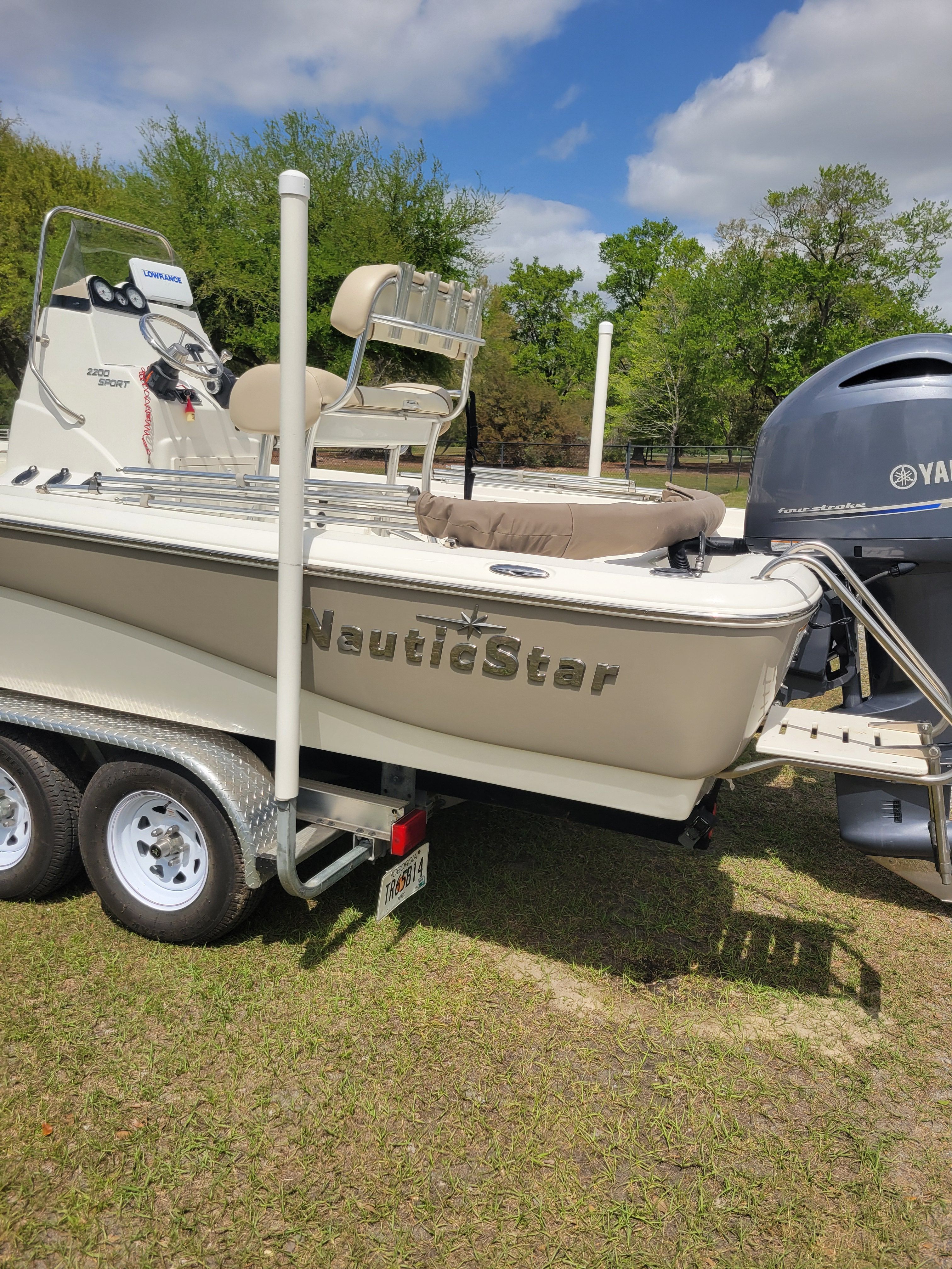A NauticStar 2200 Sport boat on a trailer, surrounded by trees and grass.