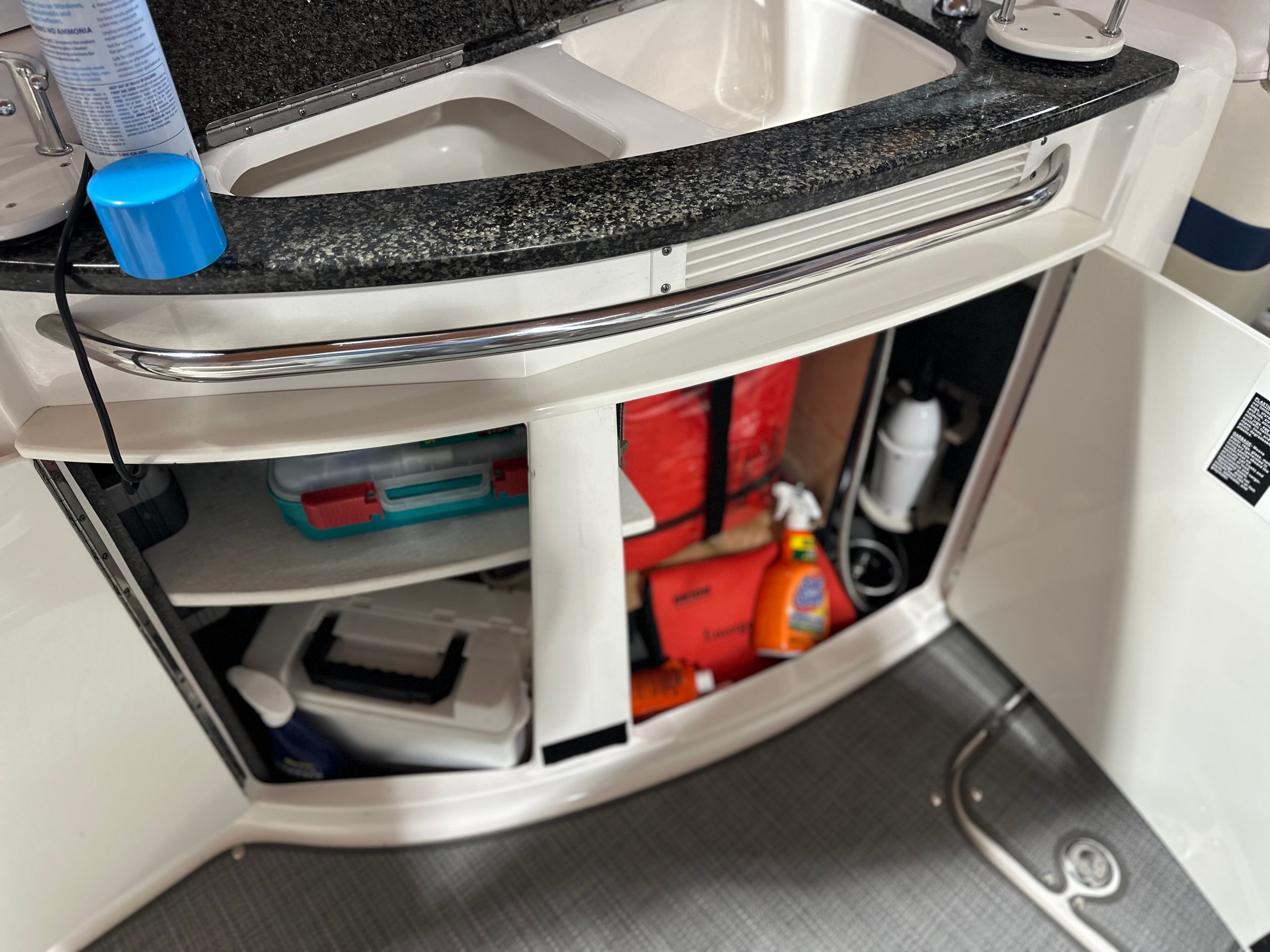 A sink with an open cabinet door reveals cleaning supplies and accessories.
