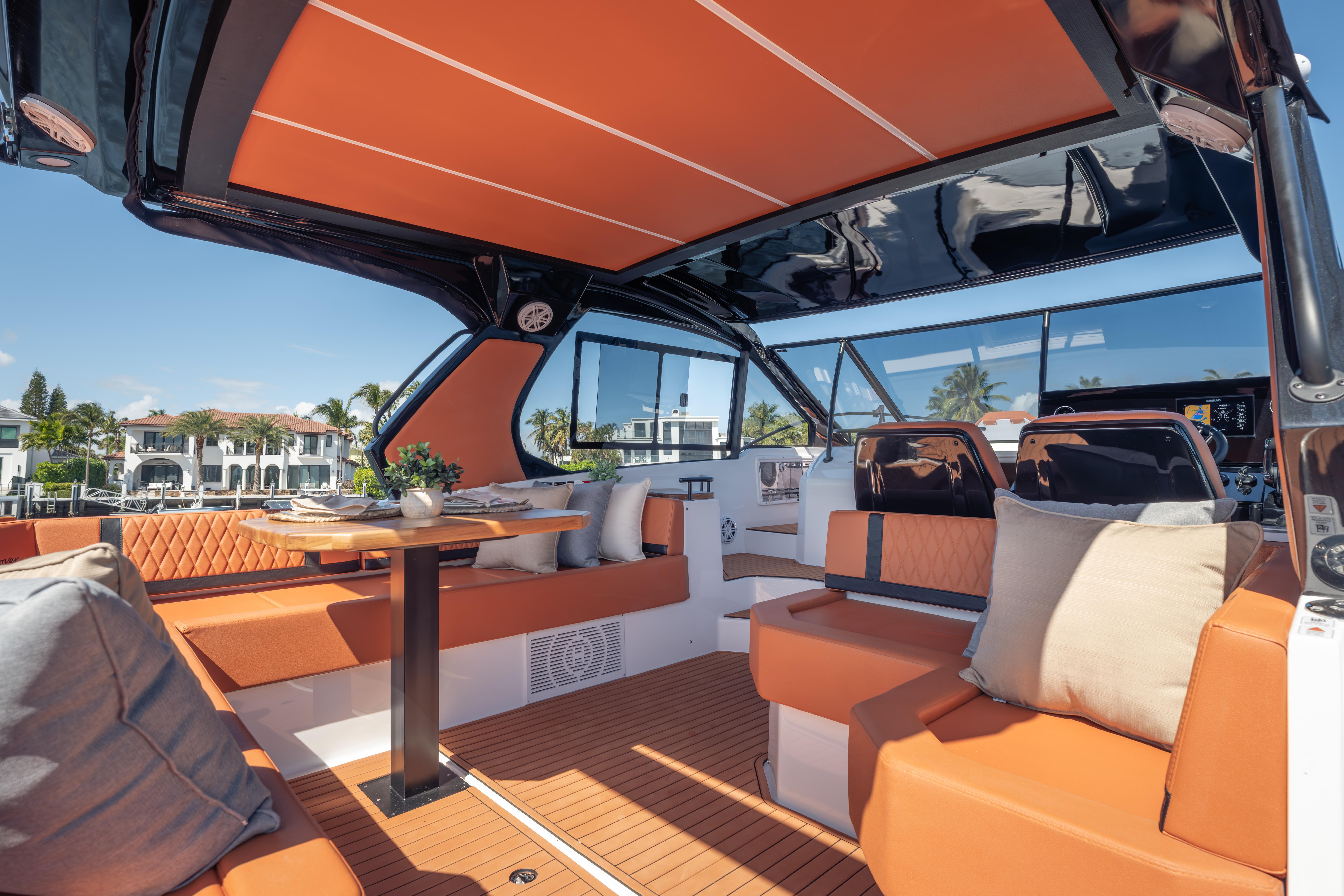 Luxurious 2026 Hanover 387 yacht interior with orange seating, elegant table, and scenic waterfront view.