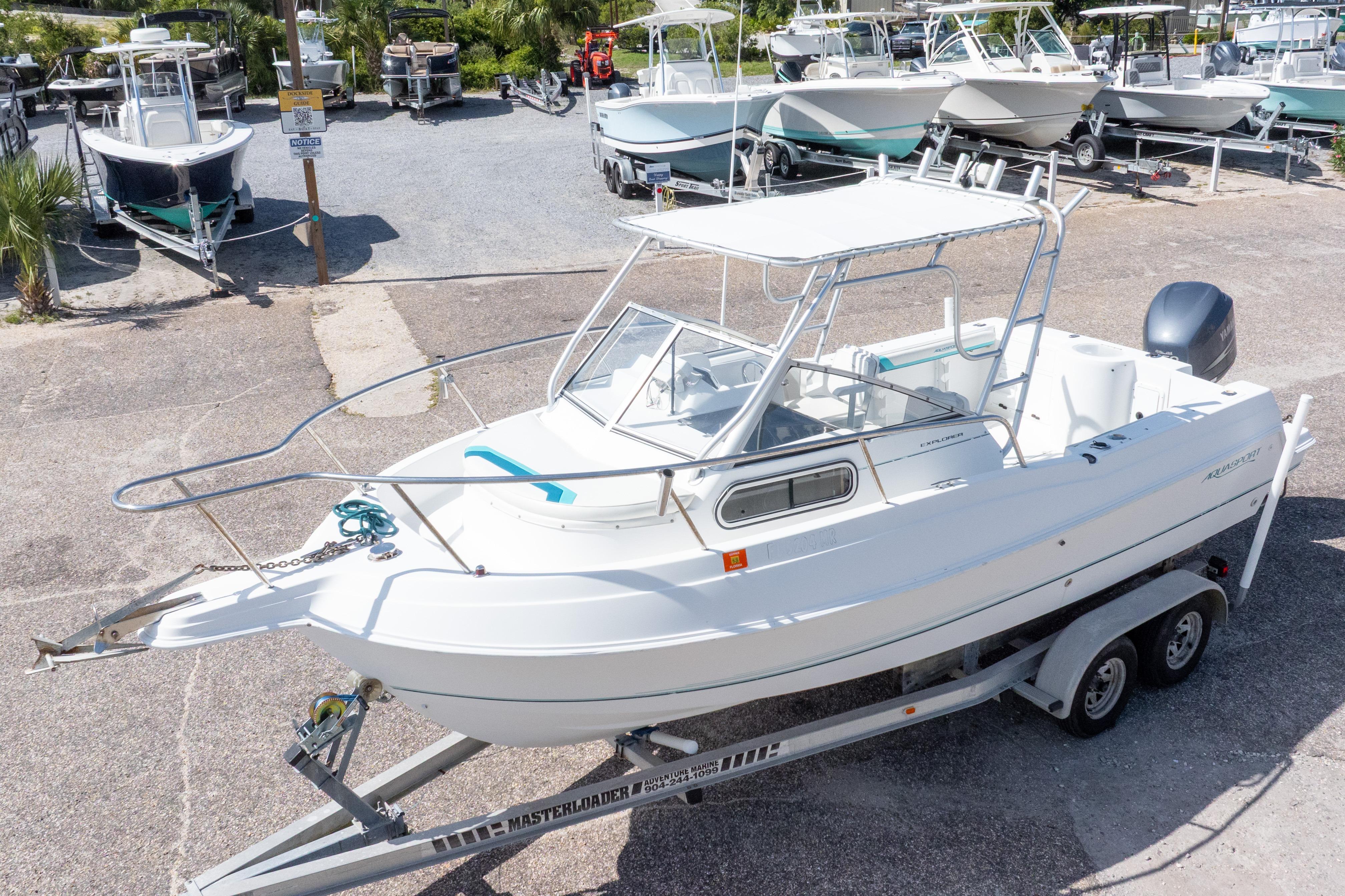 1999 Aquasport 225 Explorer boat on trailer, parked in a marina with other boats.