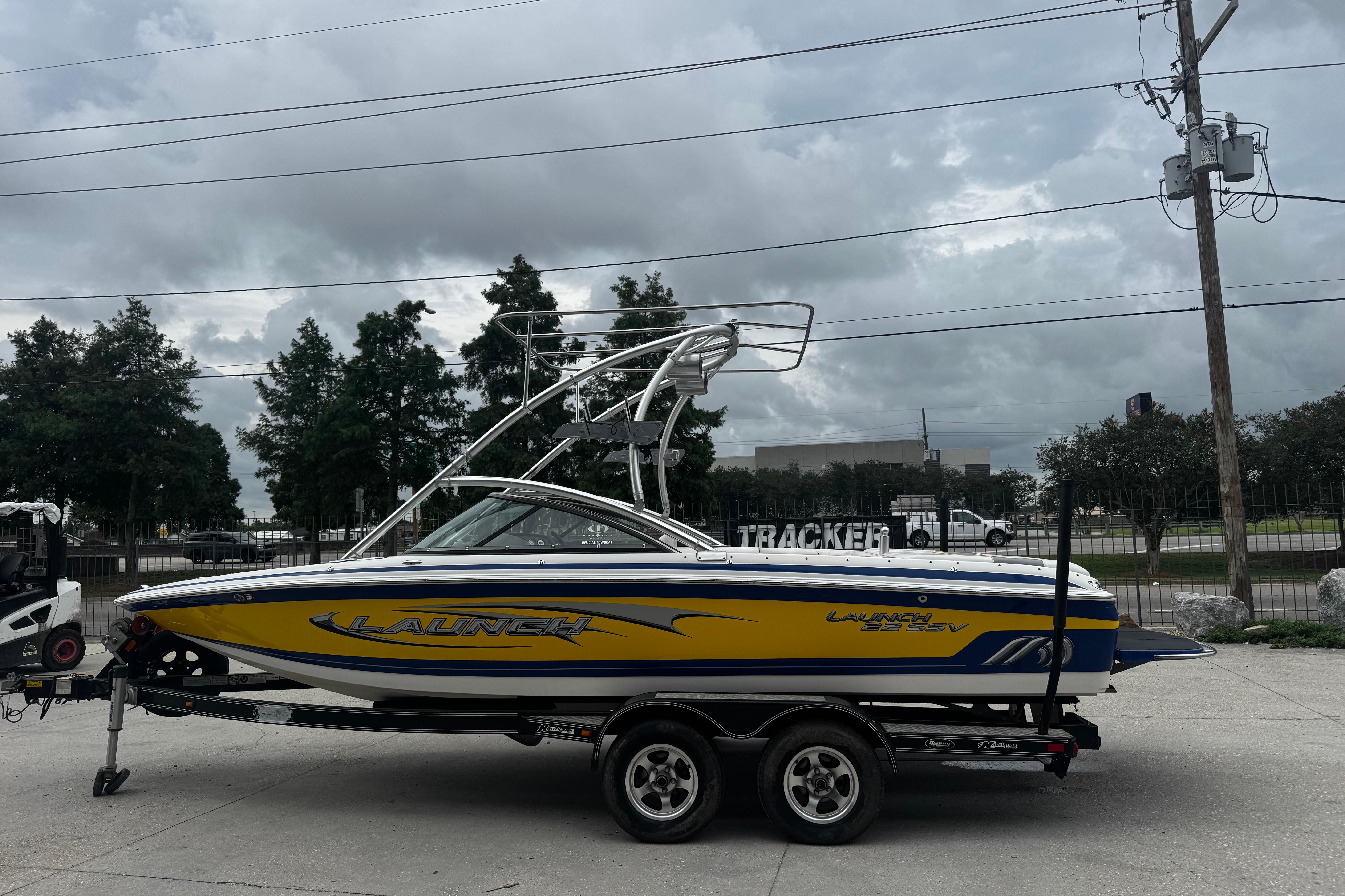 2006 Supra Launch 22 SSV boat on trailer, yellow and blue design, parked outdoors.