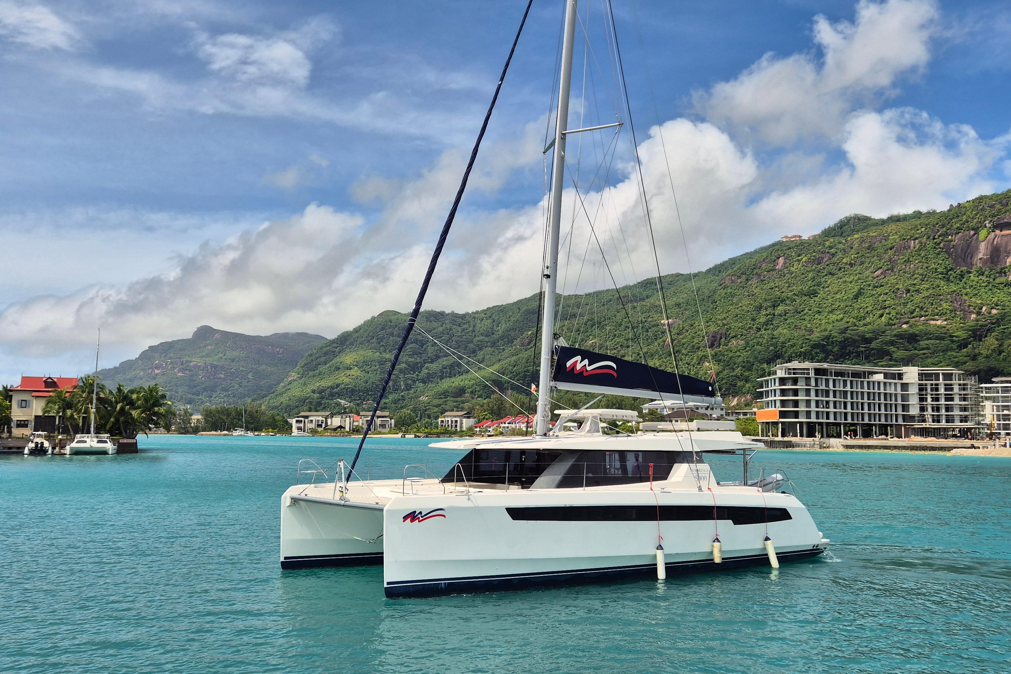 2021 Leopard 50 catamaran sailing in turquoise waters with lush green mountains in the background.