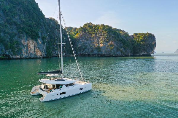 2025 Lagoon 42 Millenium catamaran sailing in scenic, tropical waters near lush cliffs.