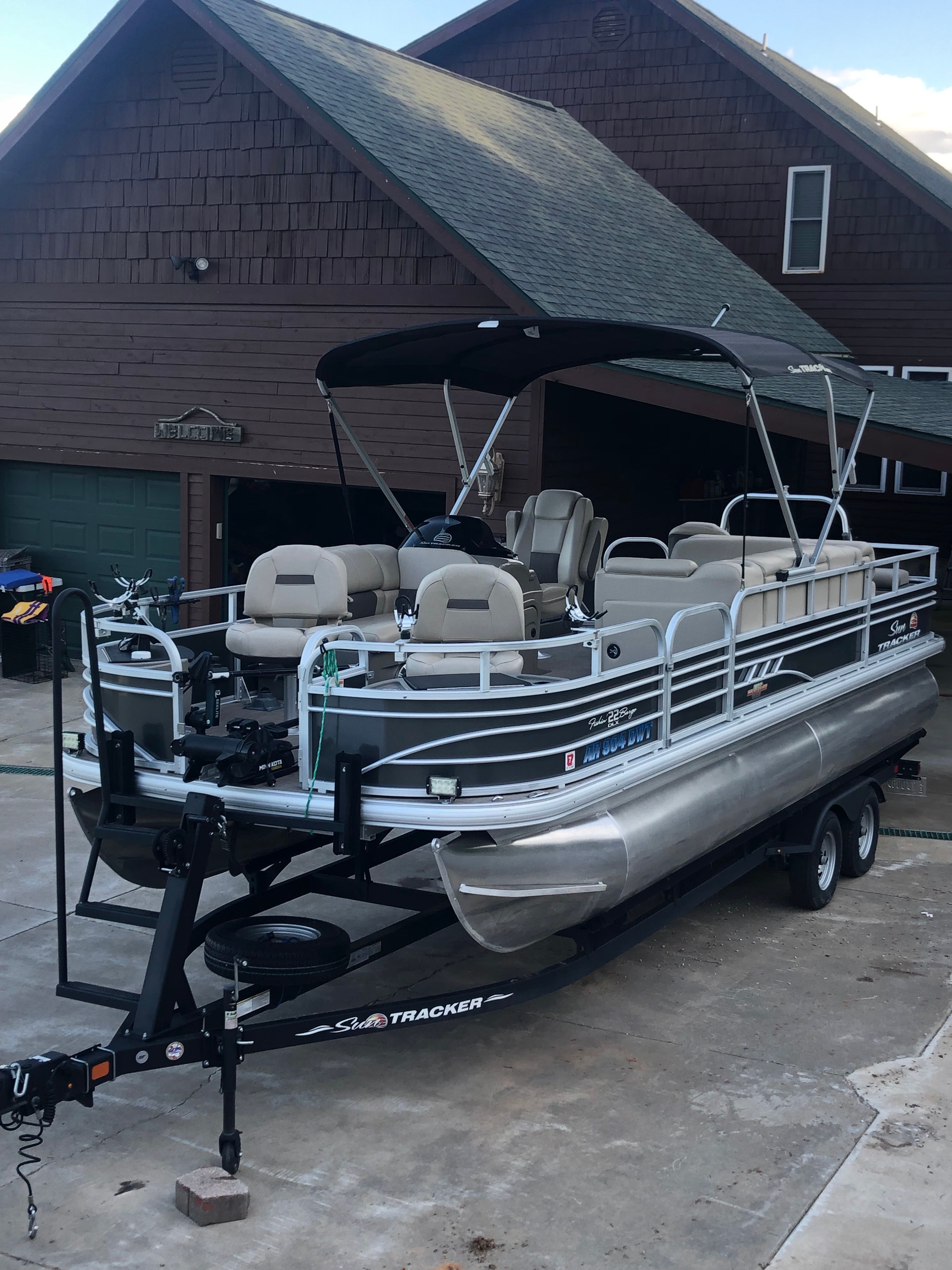 A 2023 Sun Tracker Fishin' Barge 22 DLX on a trailer in front of a house.