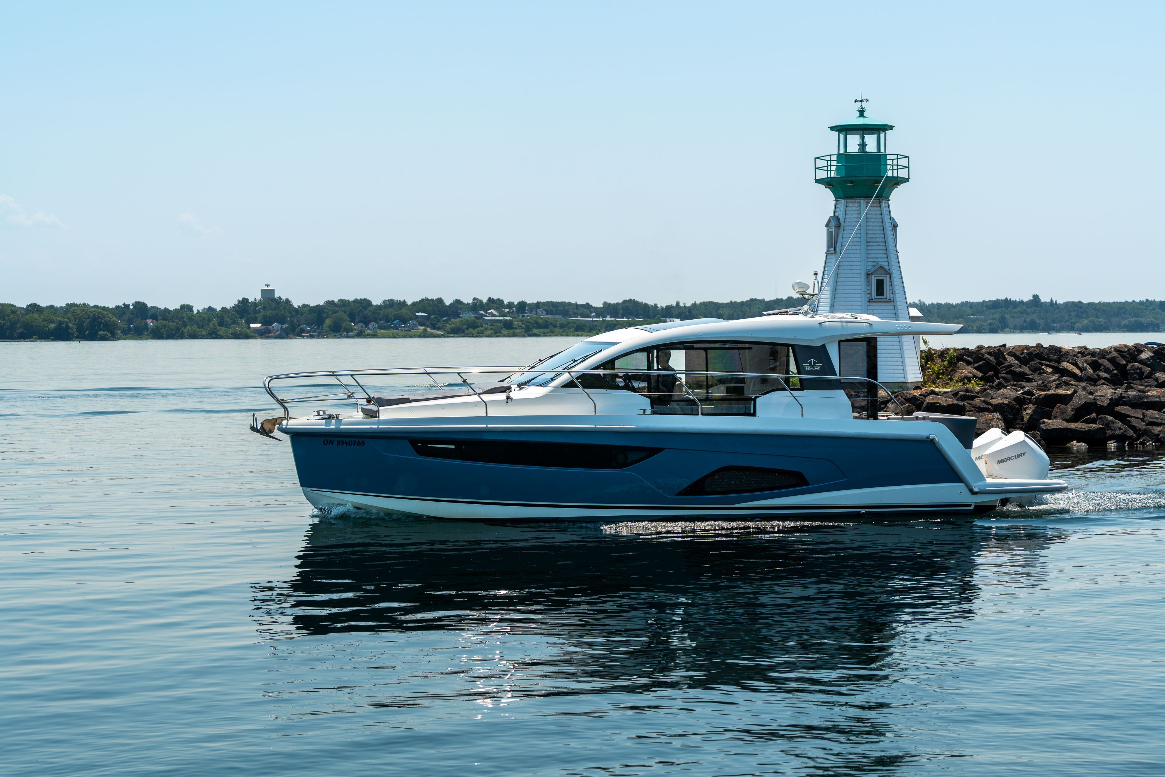 A modern Sealine C335V yacht cruises past a lighthouse on calm waters.