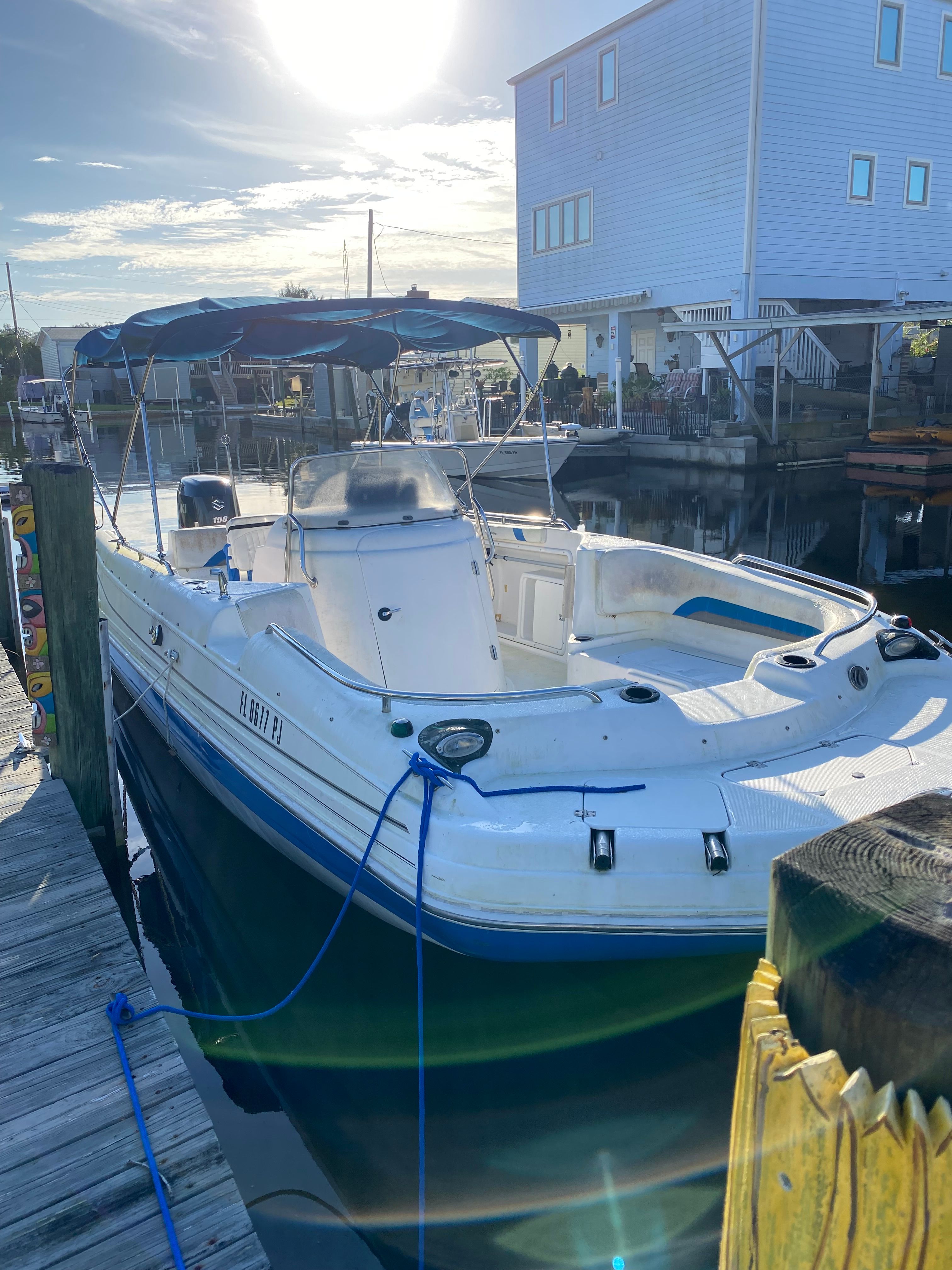 A white boat docked with a blue canopy, under a sunny sky.