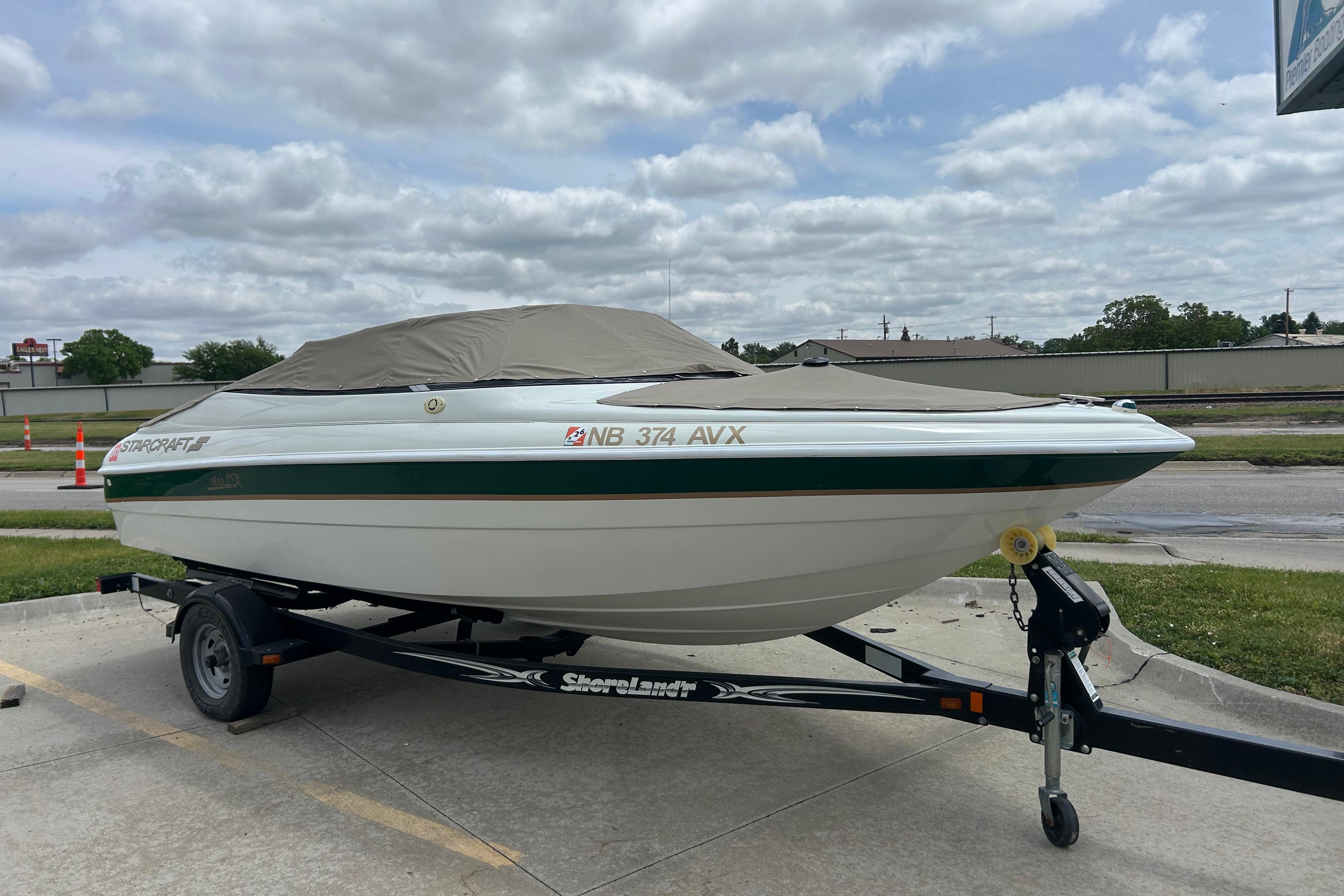 2000 Starcraft 1810 boat on trailer, covered, parked outdoors under cloudy sky.