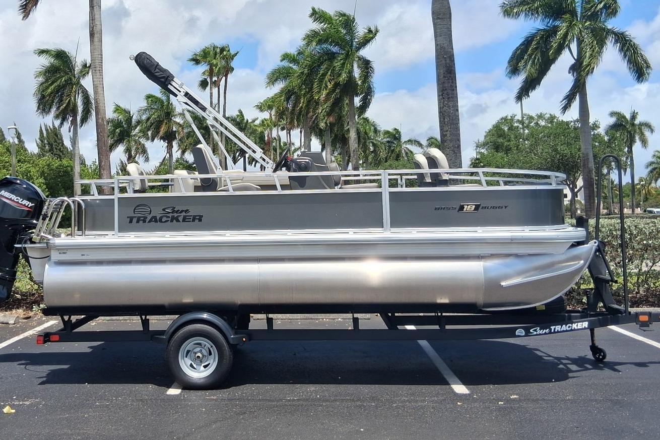 2026 Sun Tracker Bass Buggy 18 DLX pontoon boat on trailer, parked with palm trees.