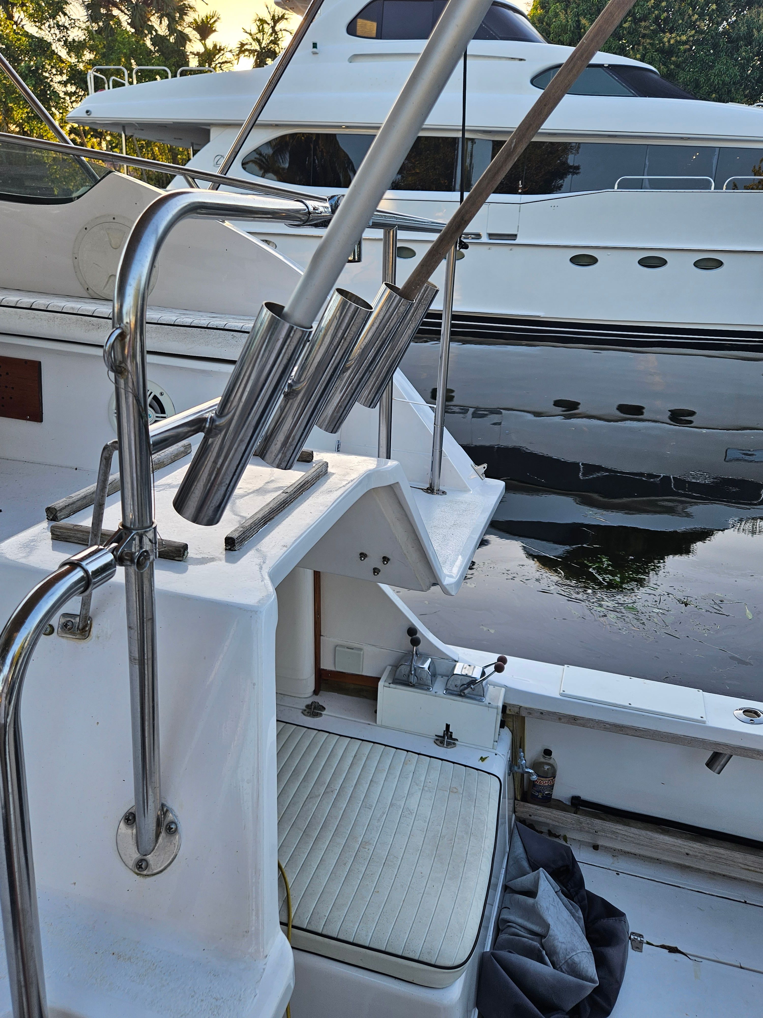 Fishing rod holders on a boat with a view of the water and another boat in the background.