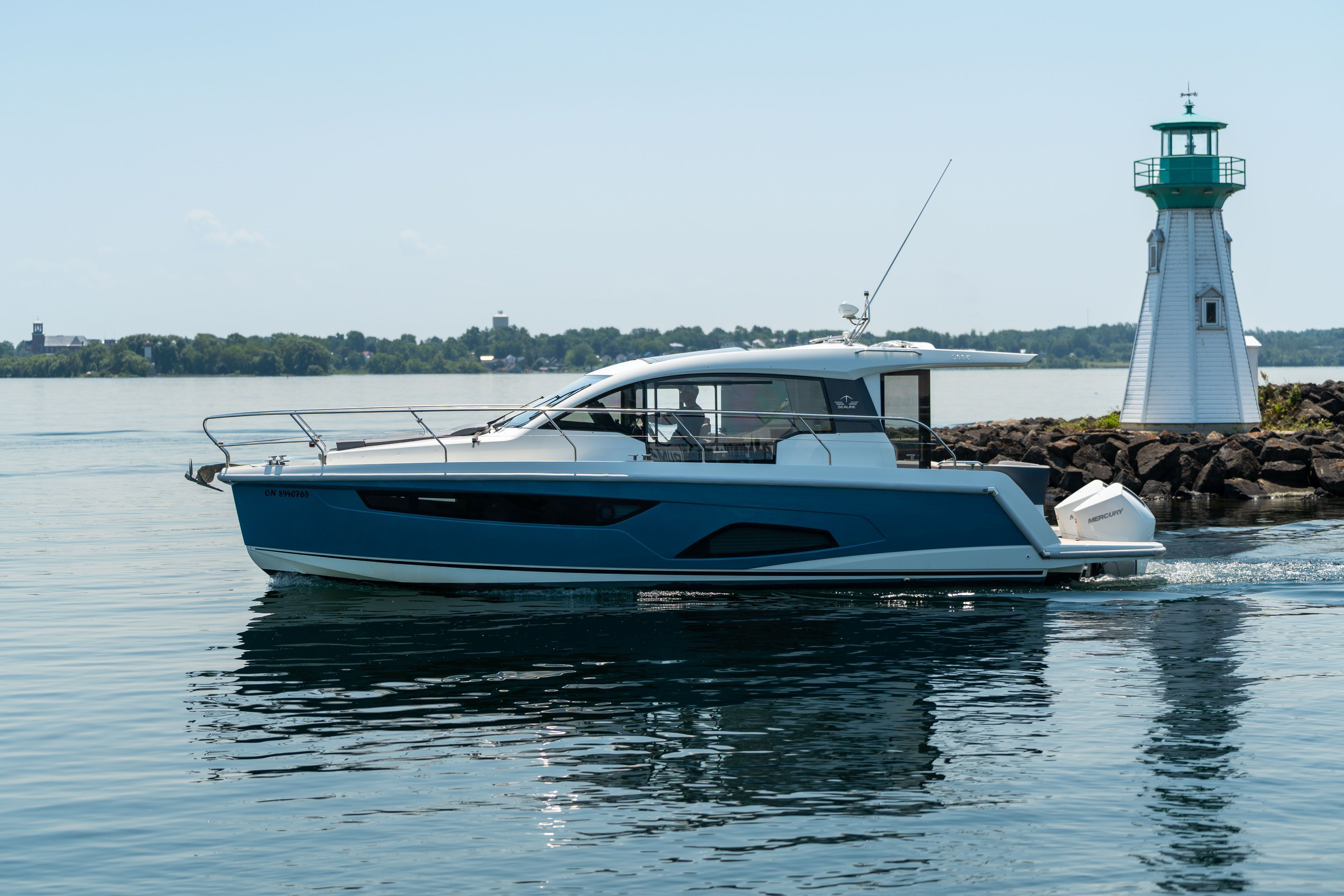 Sealine C335V 2023 cruising past a lighthouse on calm waters.