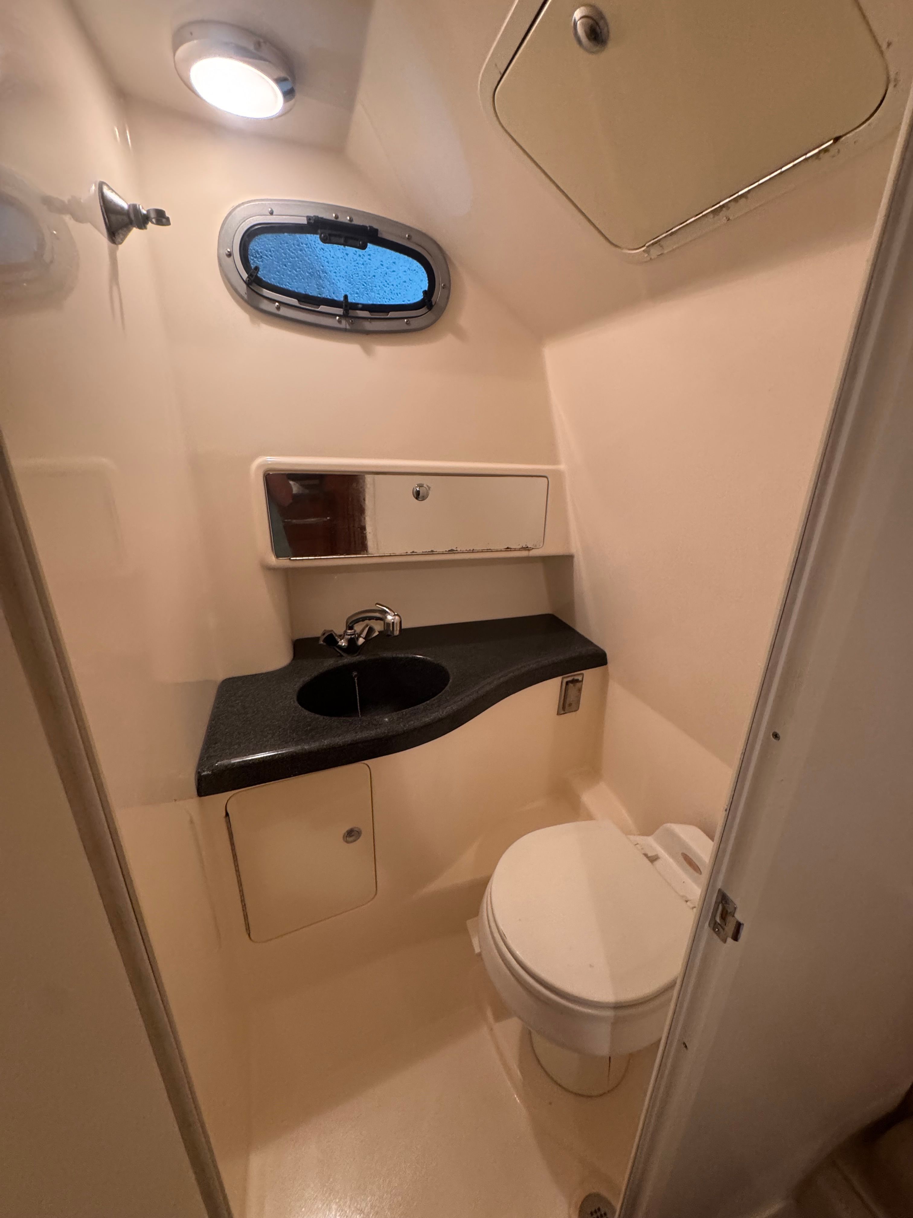 The image shows a boat bathroom with a sink, toilet, and porthole.