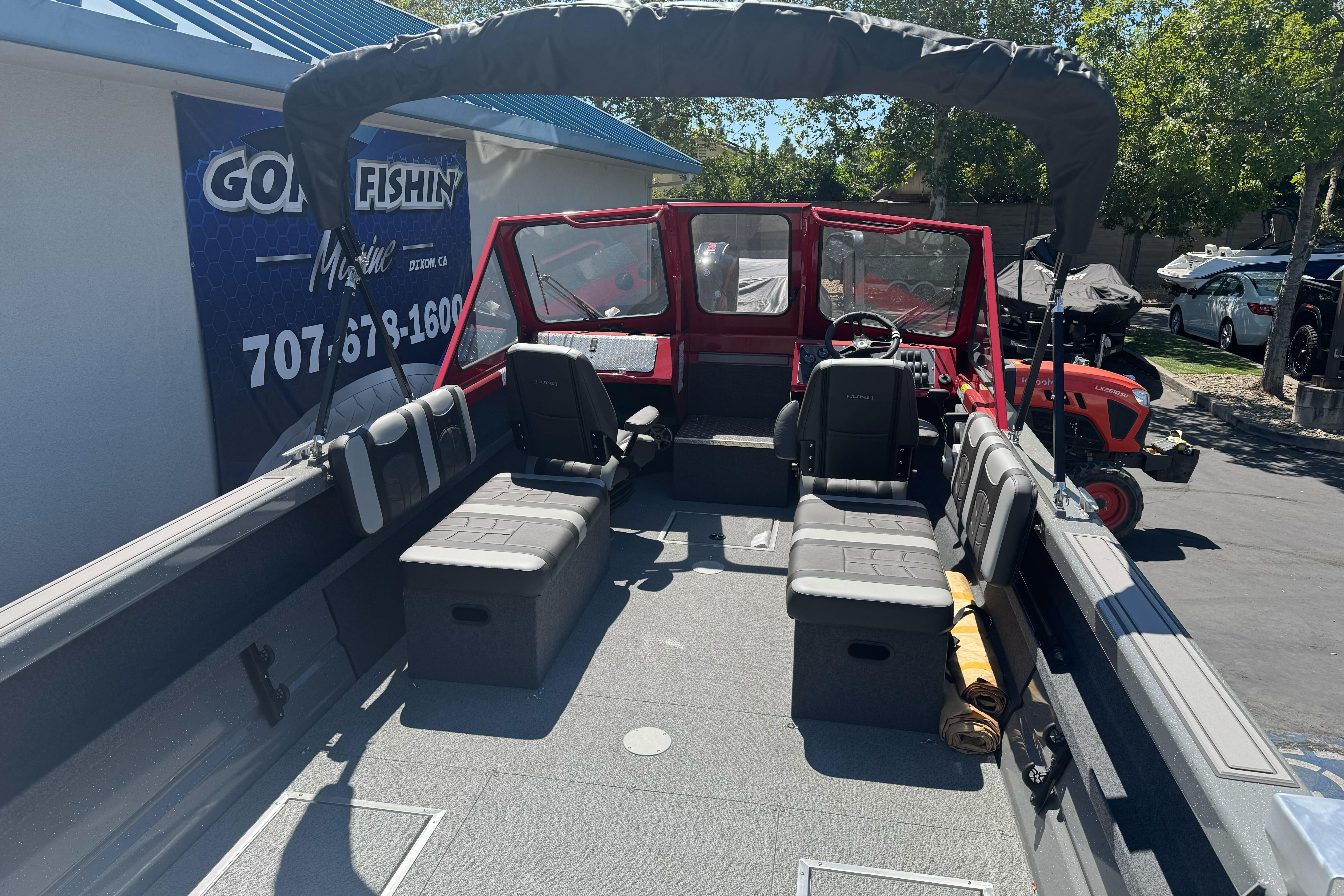 2026 Lund 210 Heavy Gauge boat interior with seating and canopy, parked outdoors.