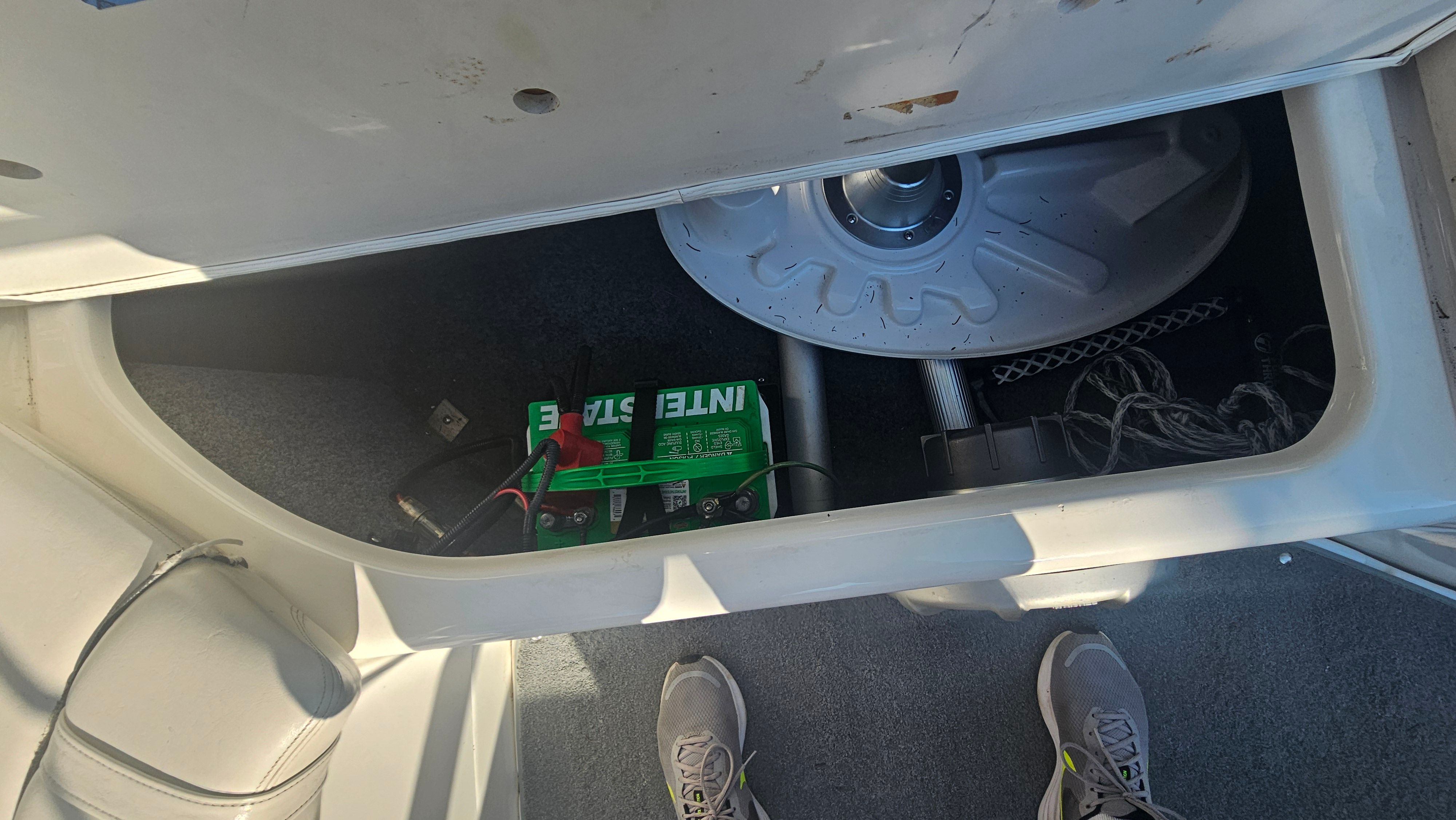 An open storage compartment on a boat reveals a battery and cables.
