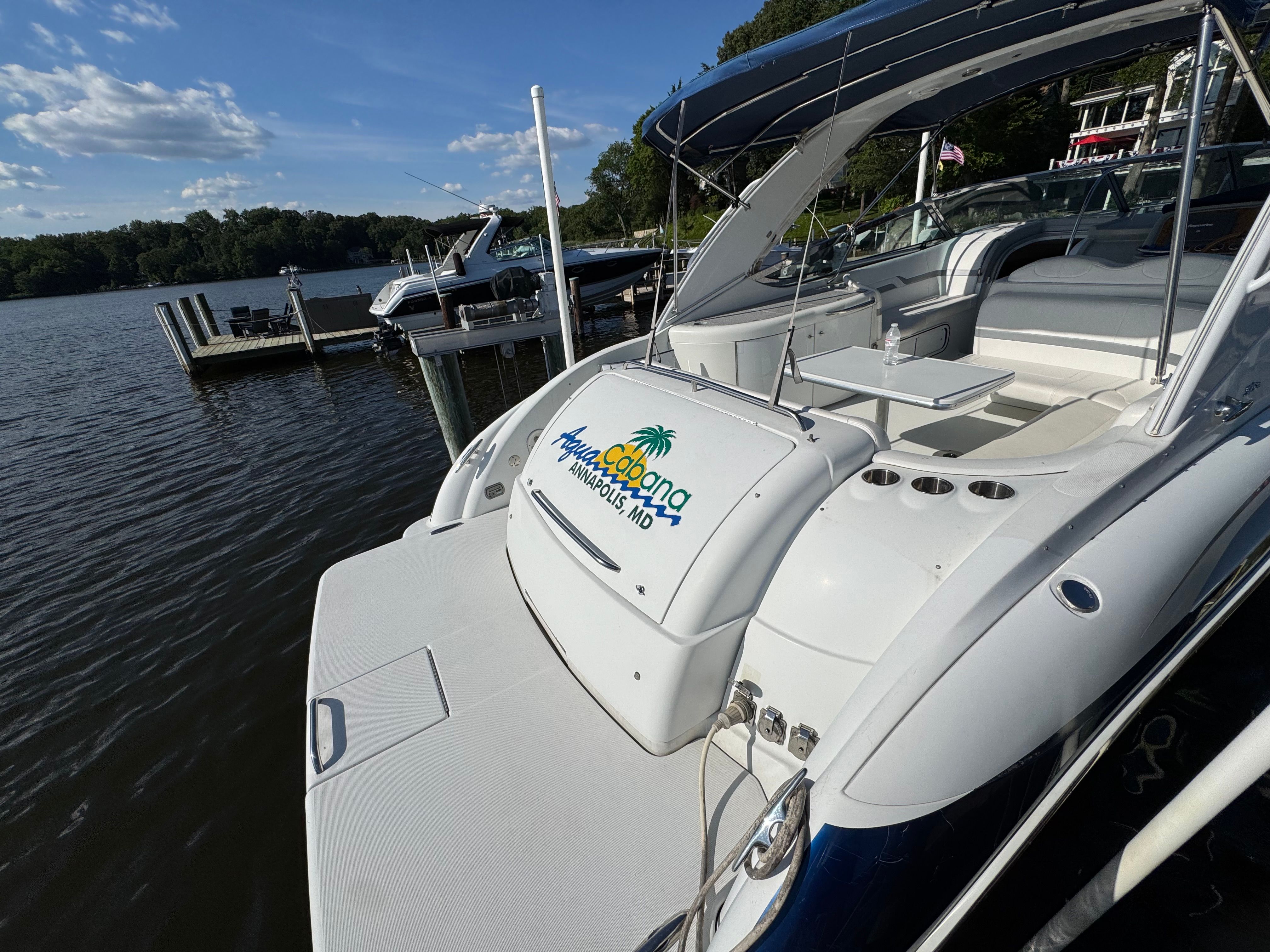 A white motorboat docked at a pier, surrounded by water and trees.