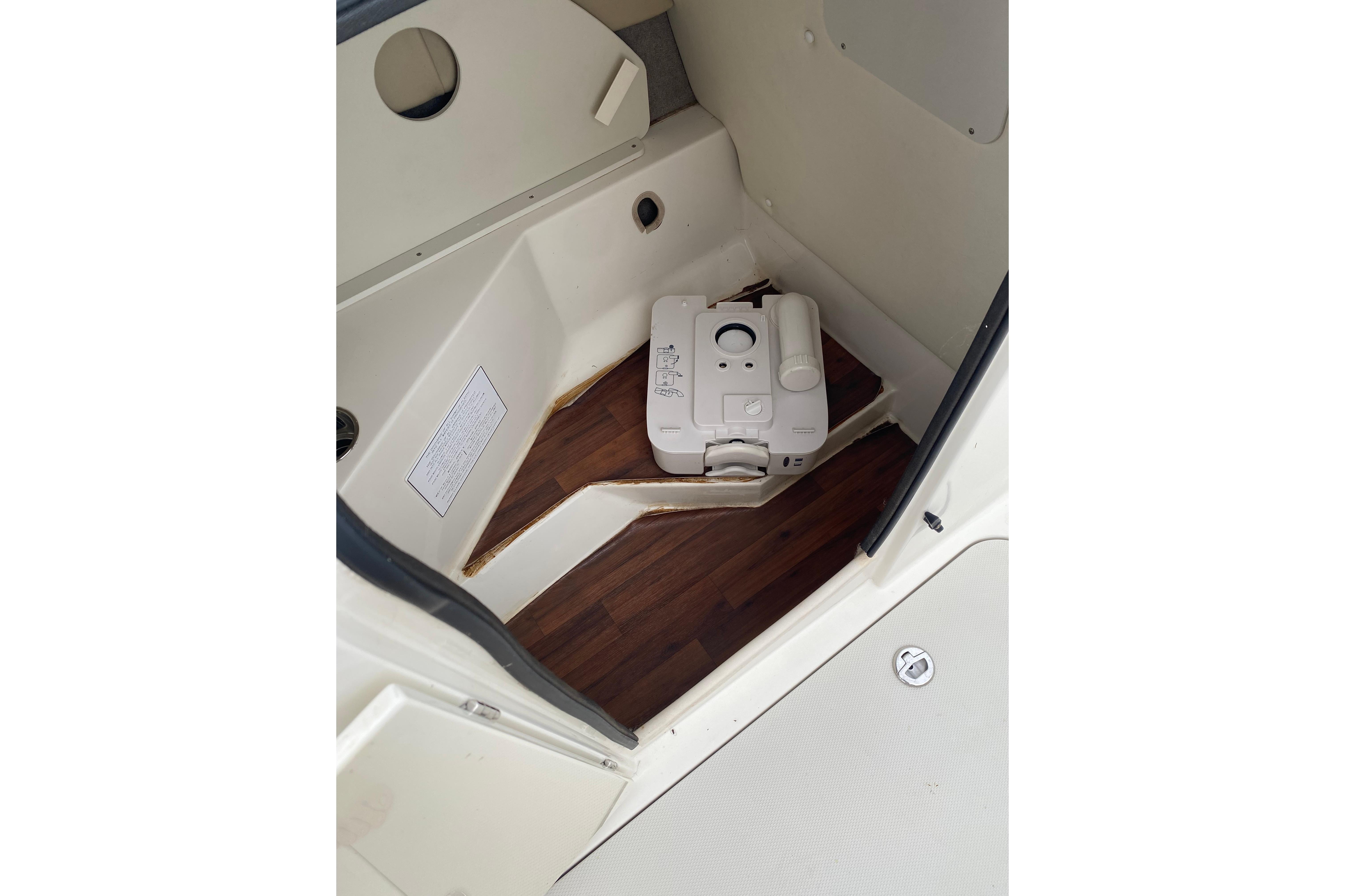 Interior of 2018 Stingray 212 SC boat with portable toilet on wooden floor.
