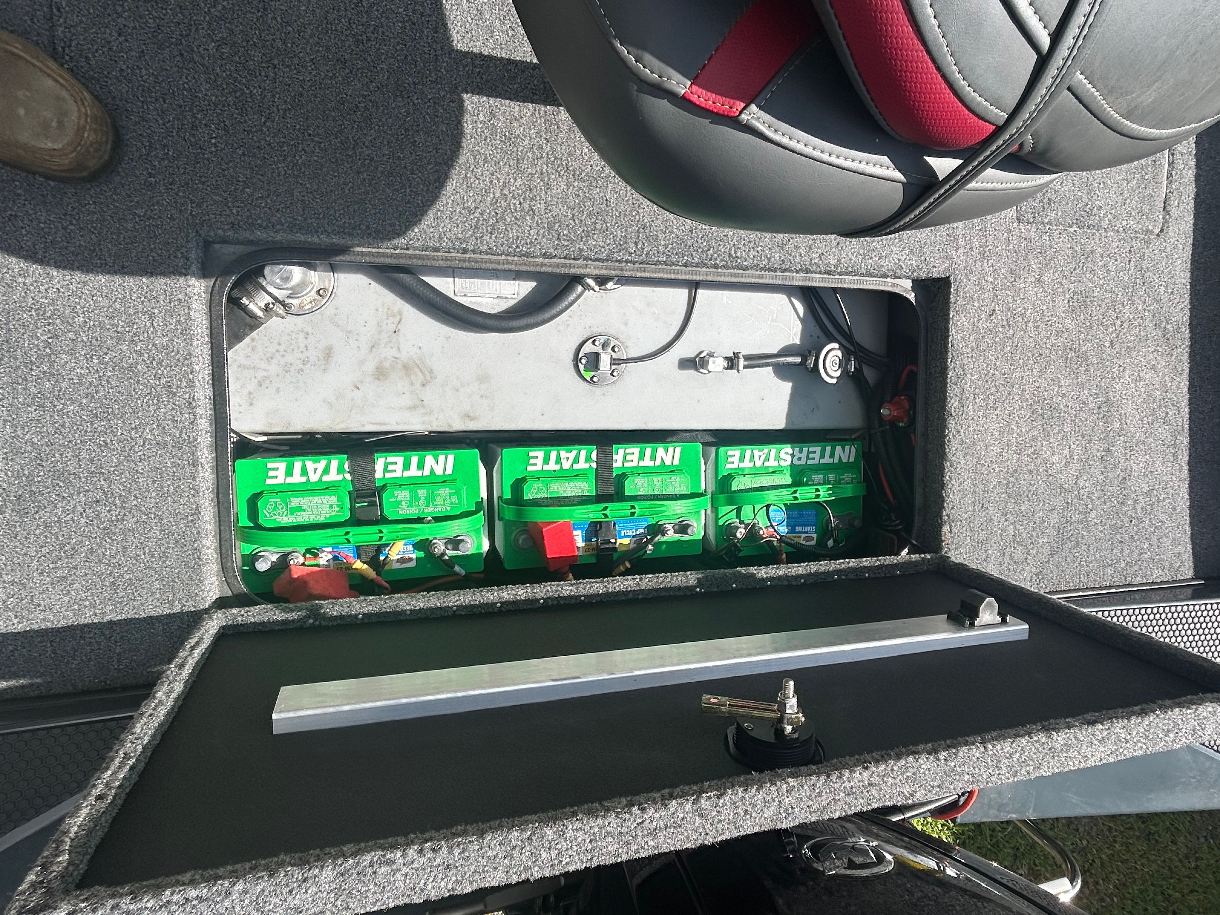 Three green batteries are visible in a compartment of a boat under a seat.