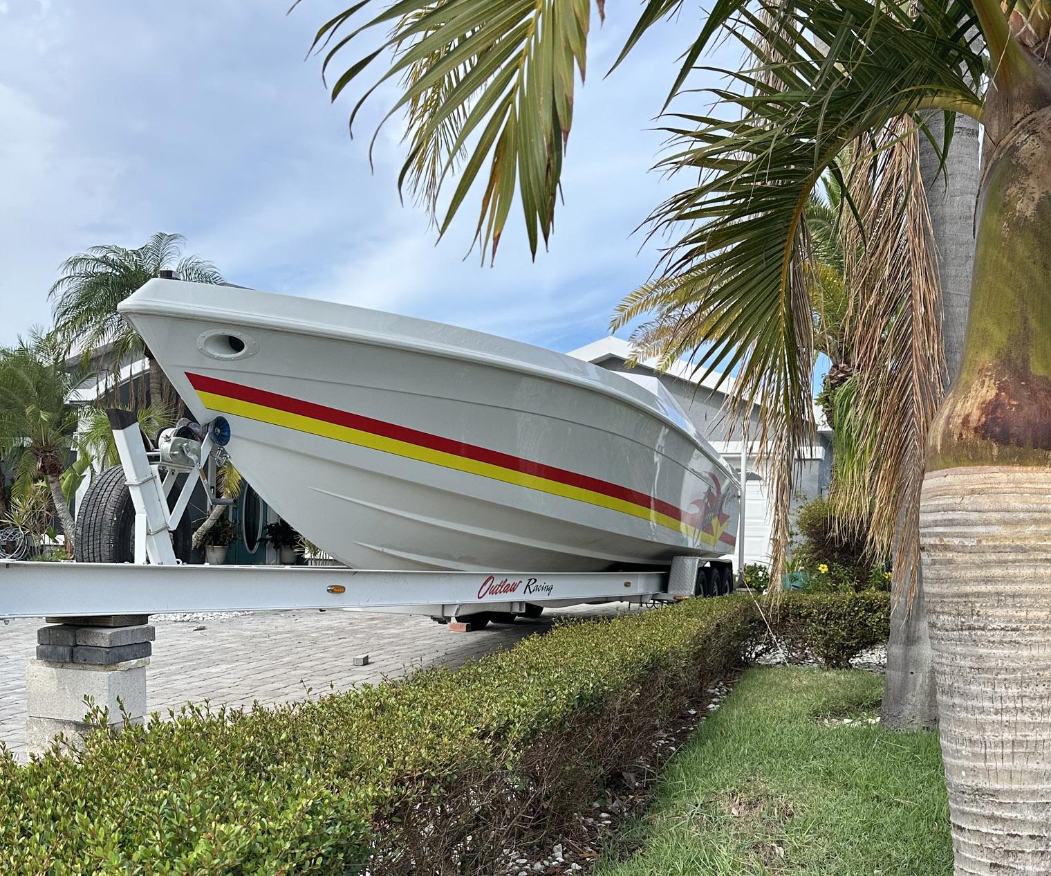 1997 Baja Outlaw 32 boat on trailer, surrounded by palm trees and greenery.
