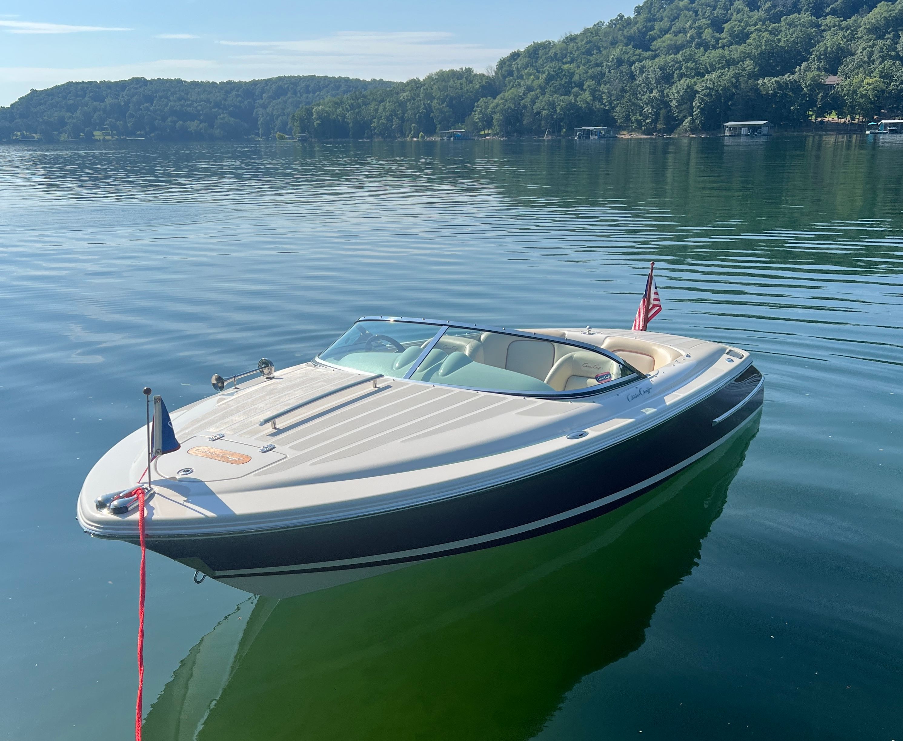 A 2006 Chris-Craft Speedster 20 floats on calm water near a wooded shoreline.