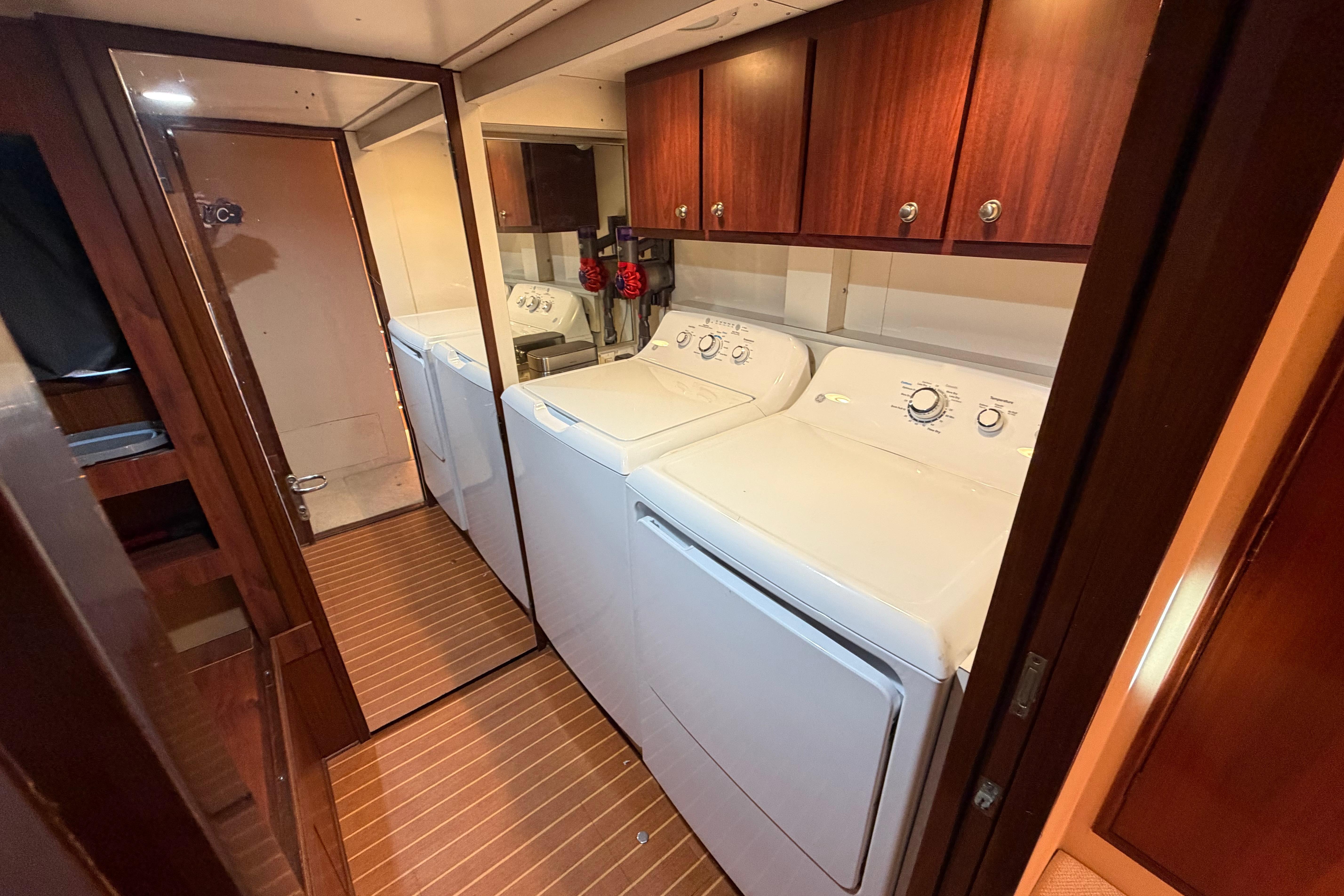 Laundry area inside 1991 Hatteras 70 Motor Yacht with washer, dryer, and wooden cabinets.
