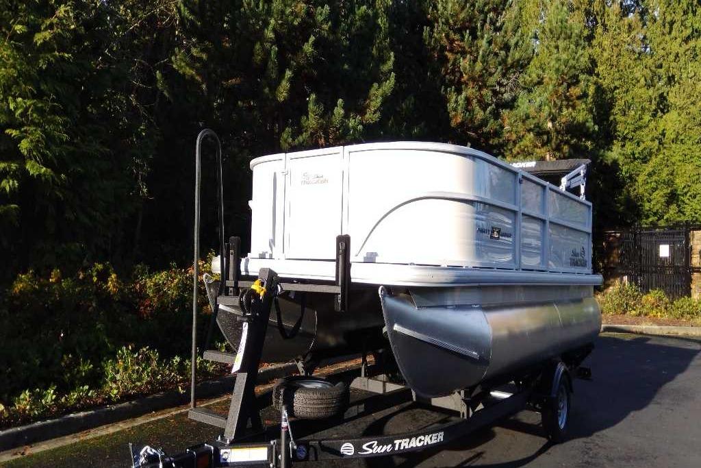 2026 Sun Tracker Party Barge 16 DLX pontoon boat on trailer, surrounded by trees.