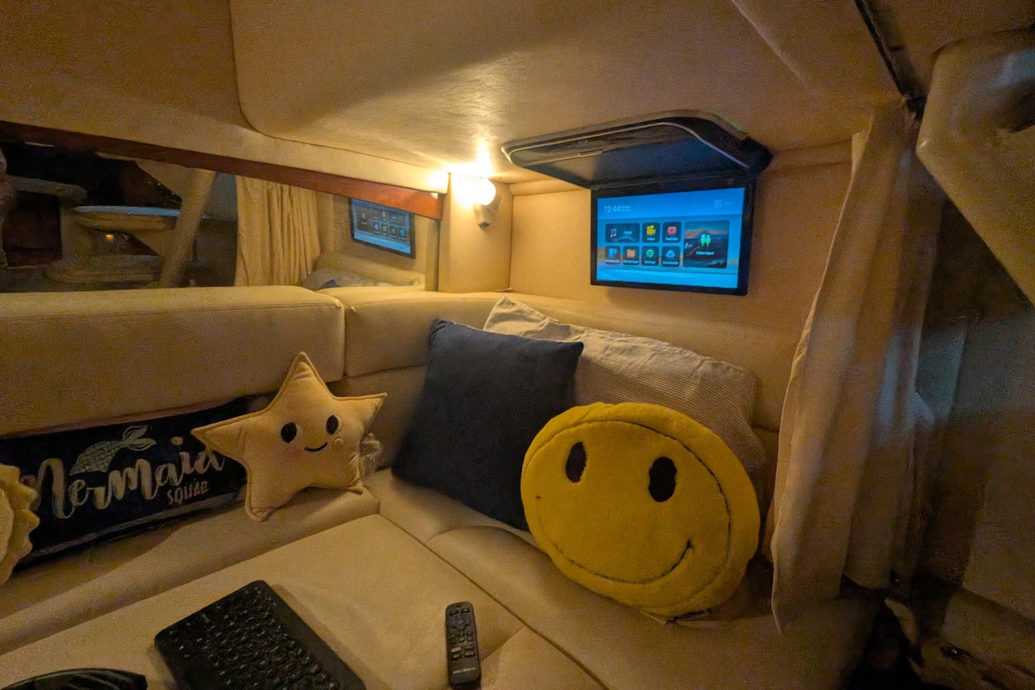 Cozy cabin interior of 2002 Sea Ray Sundancer 320 with plush pillows and wall-mounted screen.