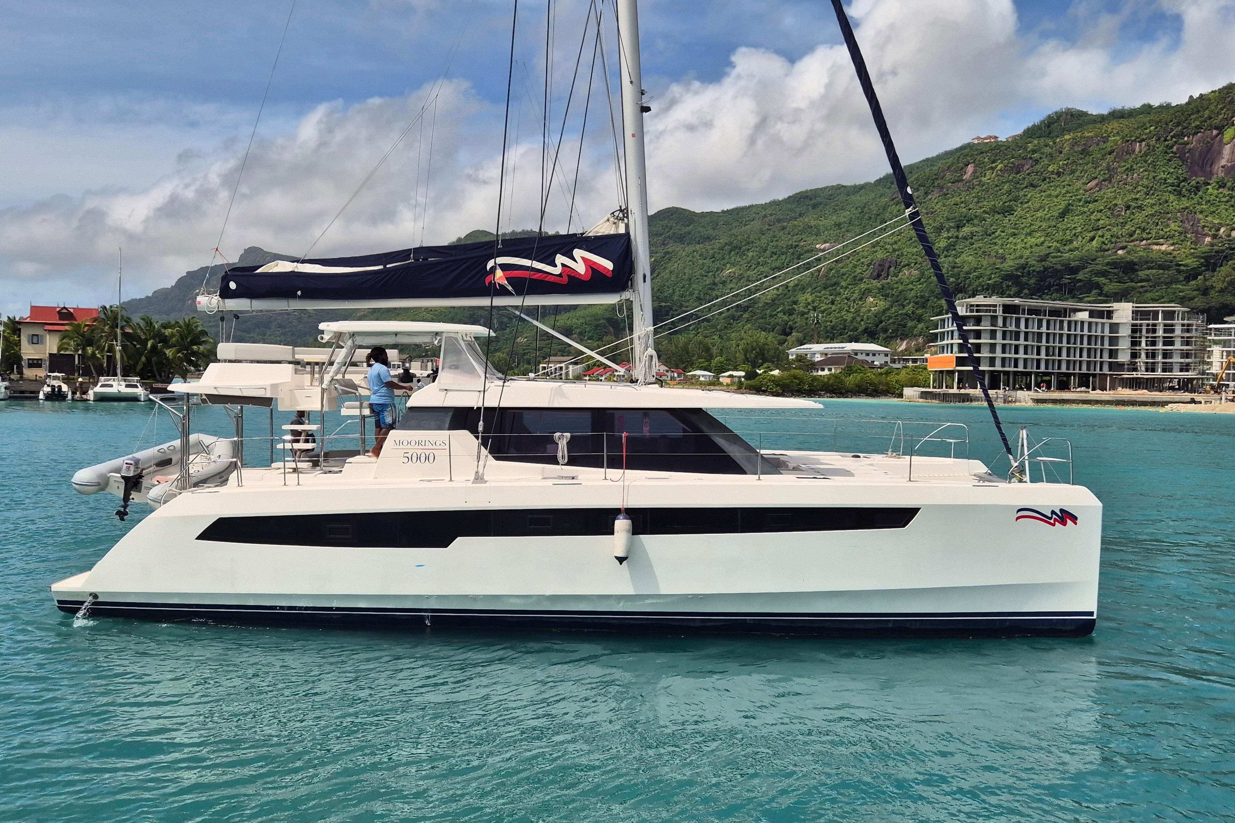 2021 Leopard 50 catamaran sailing in turquoise waters near lush green hills.