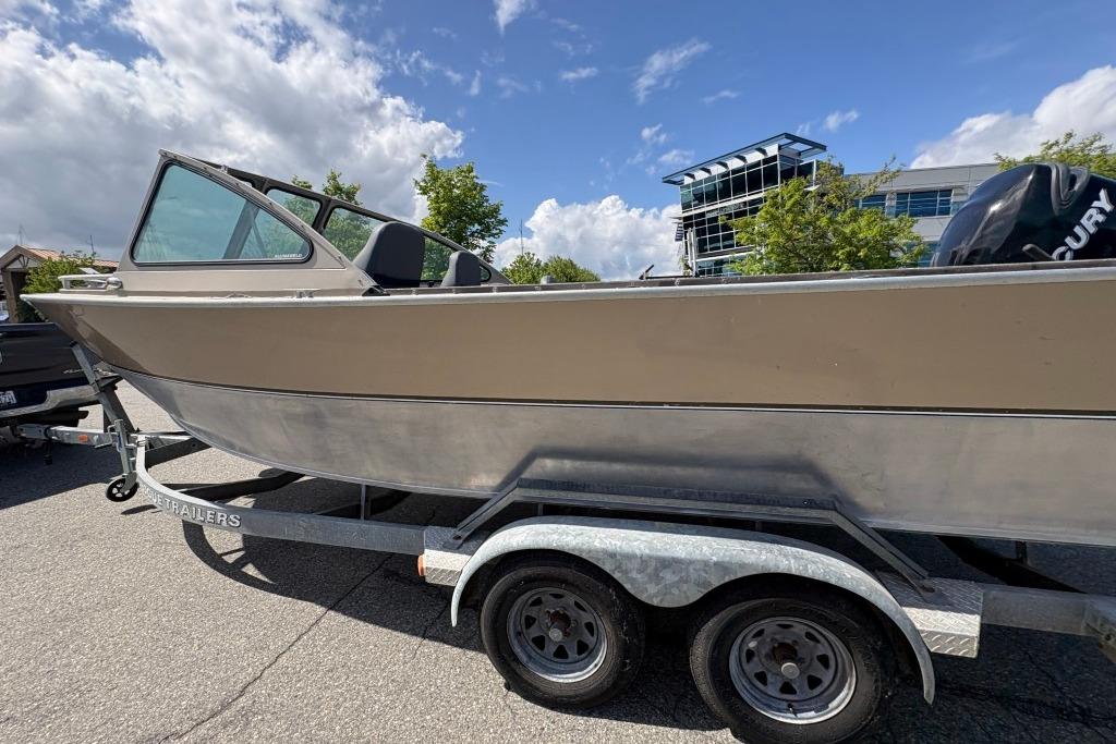 2009 Alumaweld Intruder Outboard 22 boat on trailer, parked outdoors under a cloudy sky.
