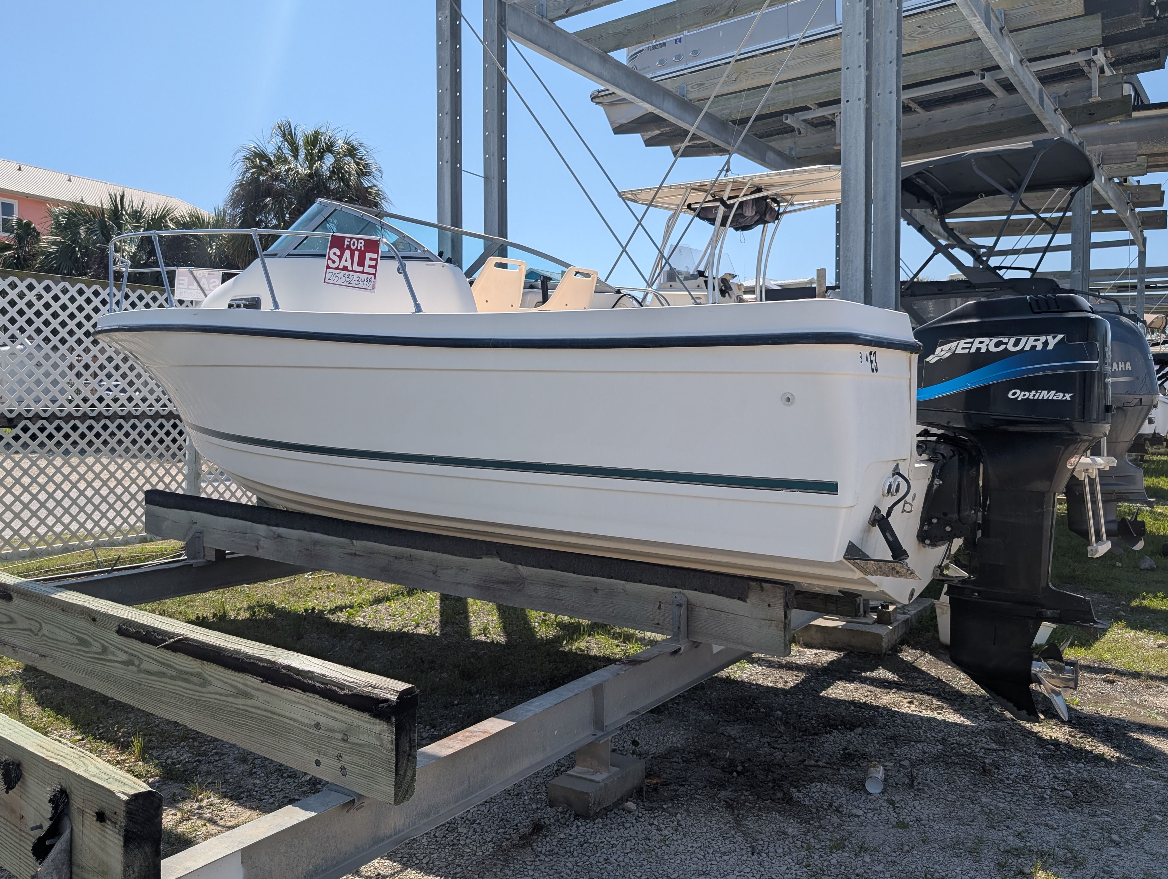 A white 2001 Trophy Bayliner boat is on a stand. A "For Sale" sign is visible.