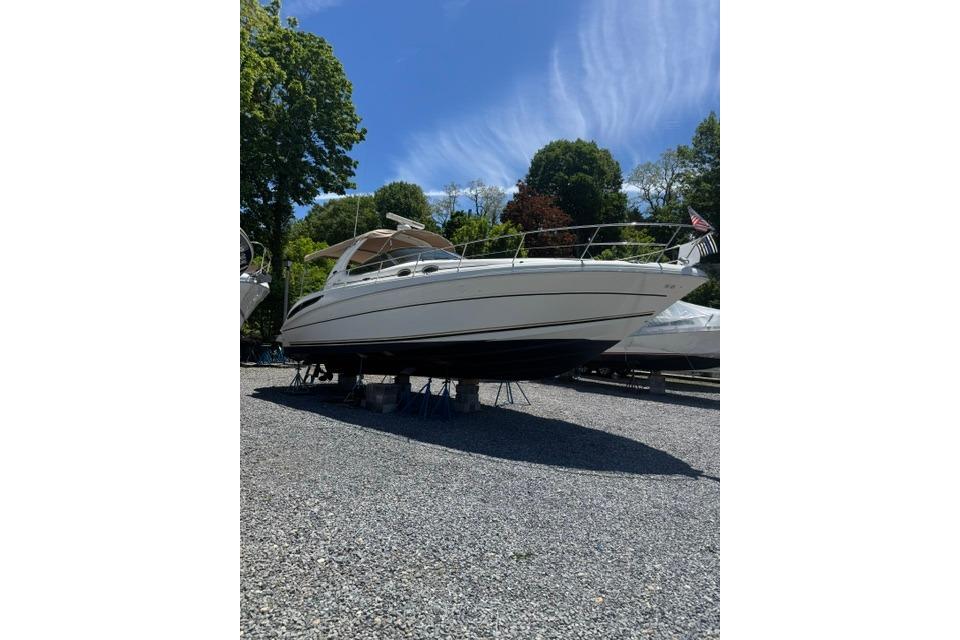 2002 Sea Ray 360 Sundancer yacht on gravel, surrounded by trees under a clear sky.