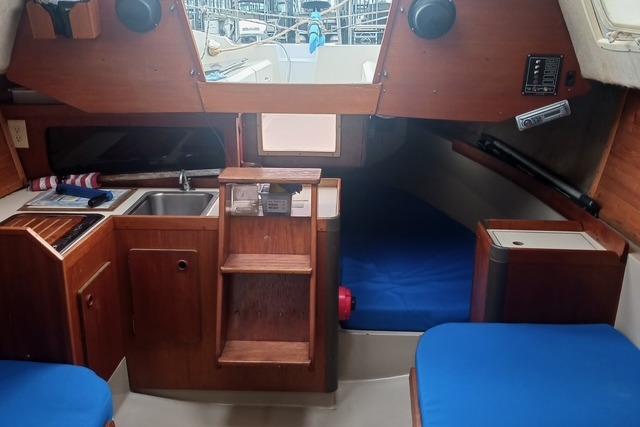 Interior of 1989 O'Day 272 sailboat with wooden cabinetry and blue cushions.