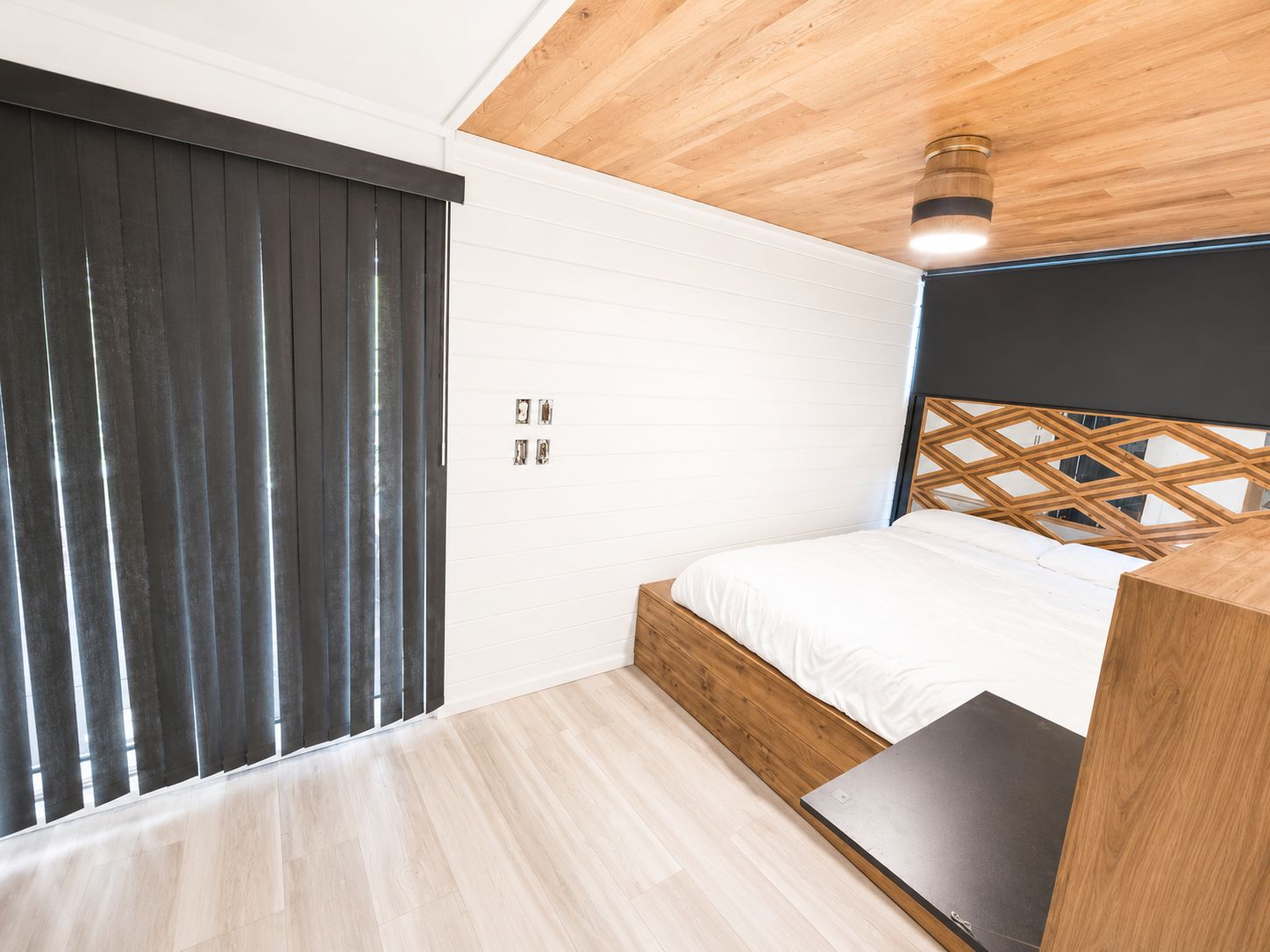 A modern bedroom with wooden floor and ceiling, a large bed, and black curtains.