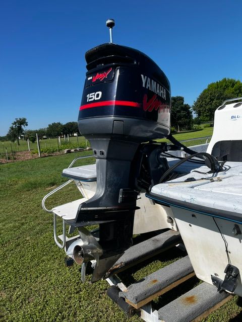 A boat with a Yamaha 150 outboard motor is on a trailer on a grassy area.