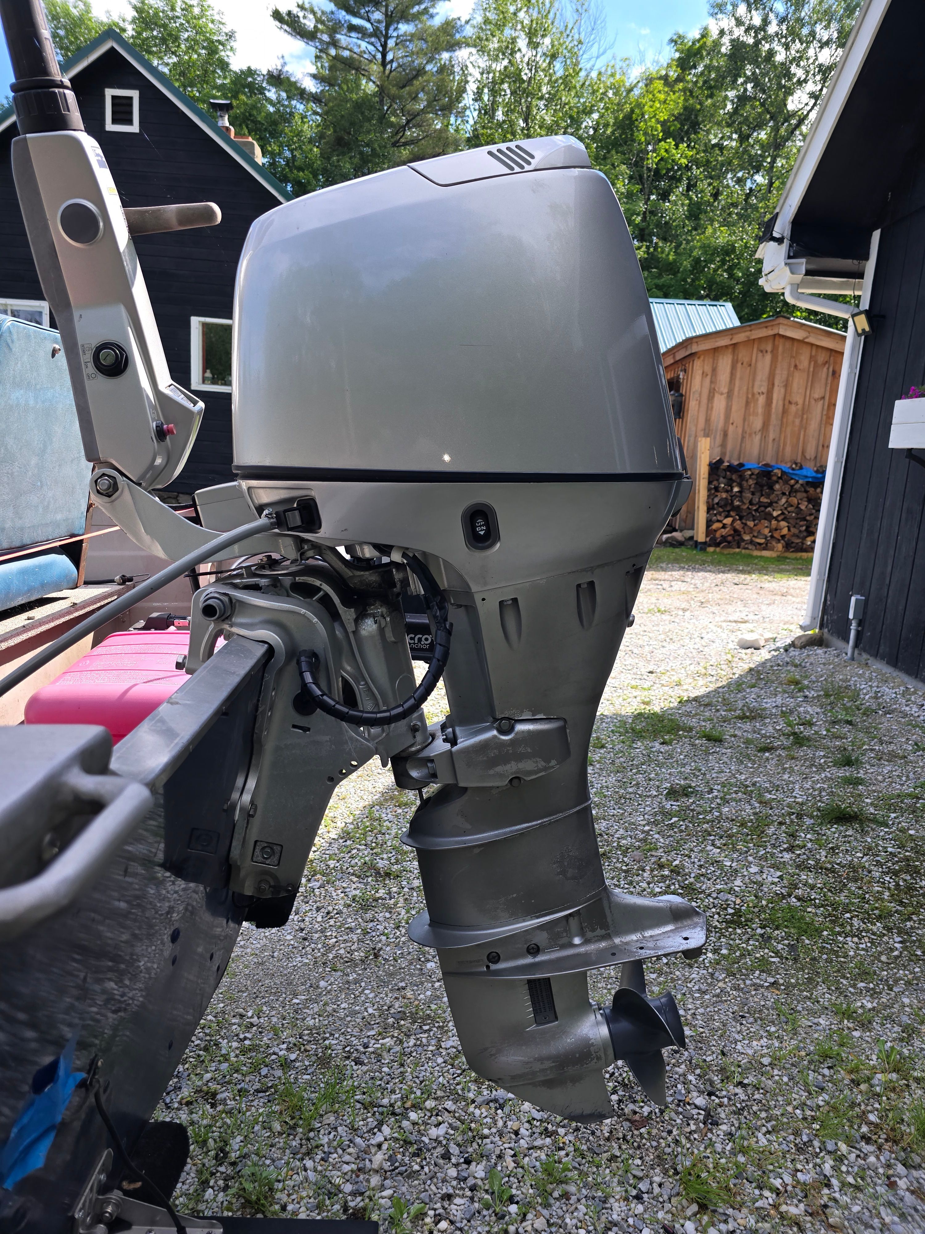 An outboard motor on a boat parked on a gravel path, with buildings in the background.
