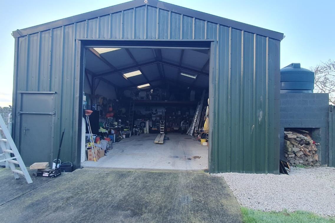 Open green metal garage with tools and equipment inside, featuring a 1989 Fairey Spearfish MKIII.