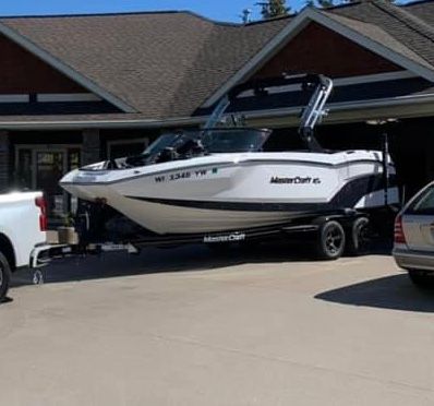 A white 2020 MasterCraft NXT22 boat on a trailer parked in front of a house.