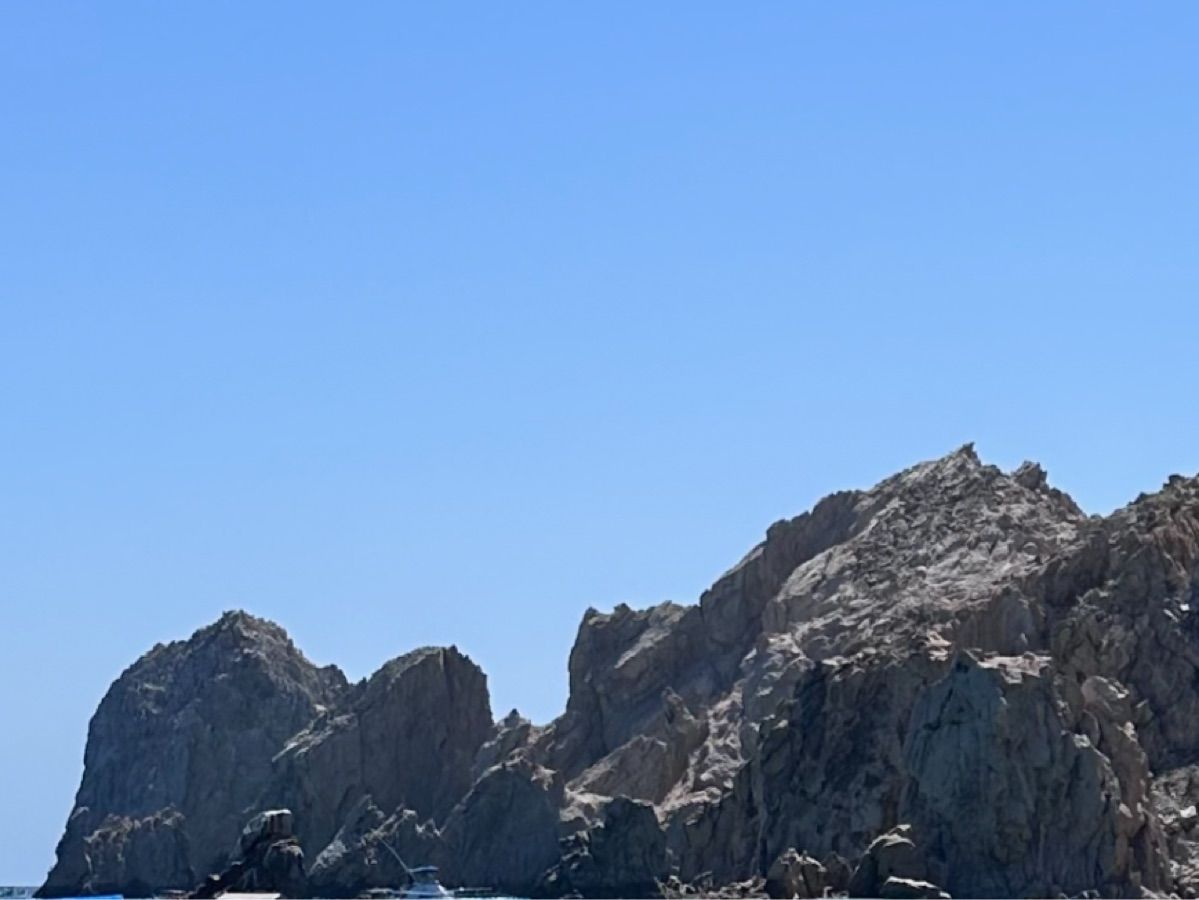 Sailboat near rocky coastline under clear sky.