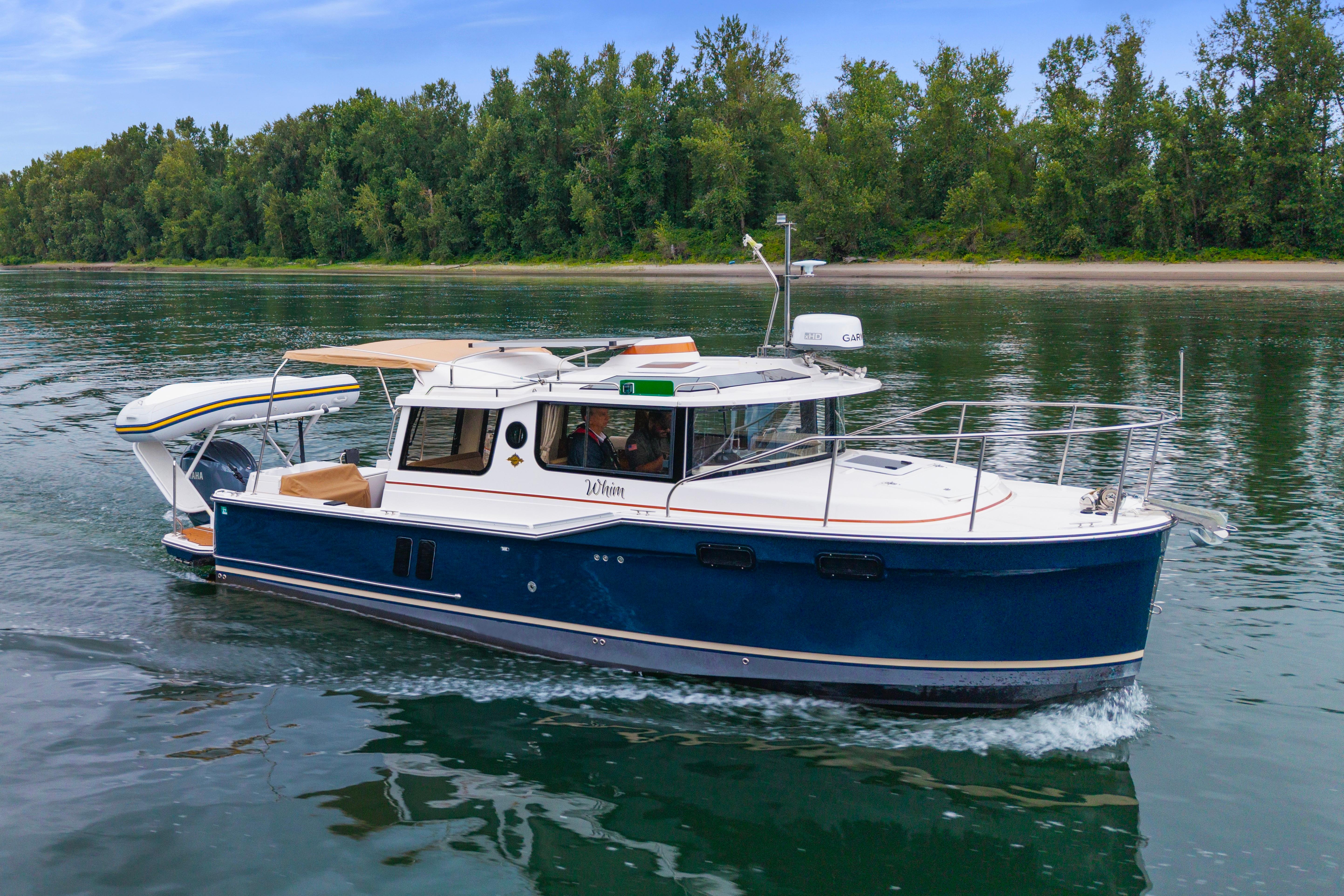 2022 Ranger Tugs R-27 cruising on a serene lake with lush green trees in the background.