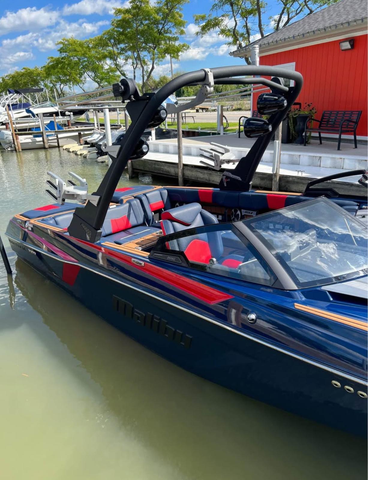 2021 Malibu Wakesetter 24 MXZ boat docked by a red building, under a clear blue sky.