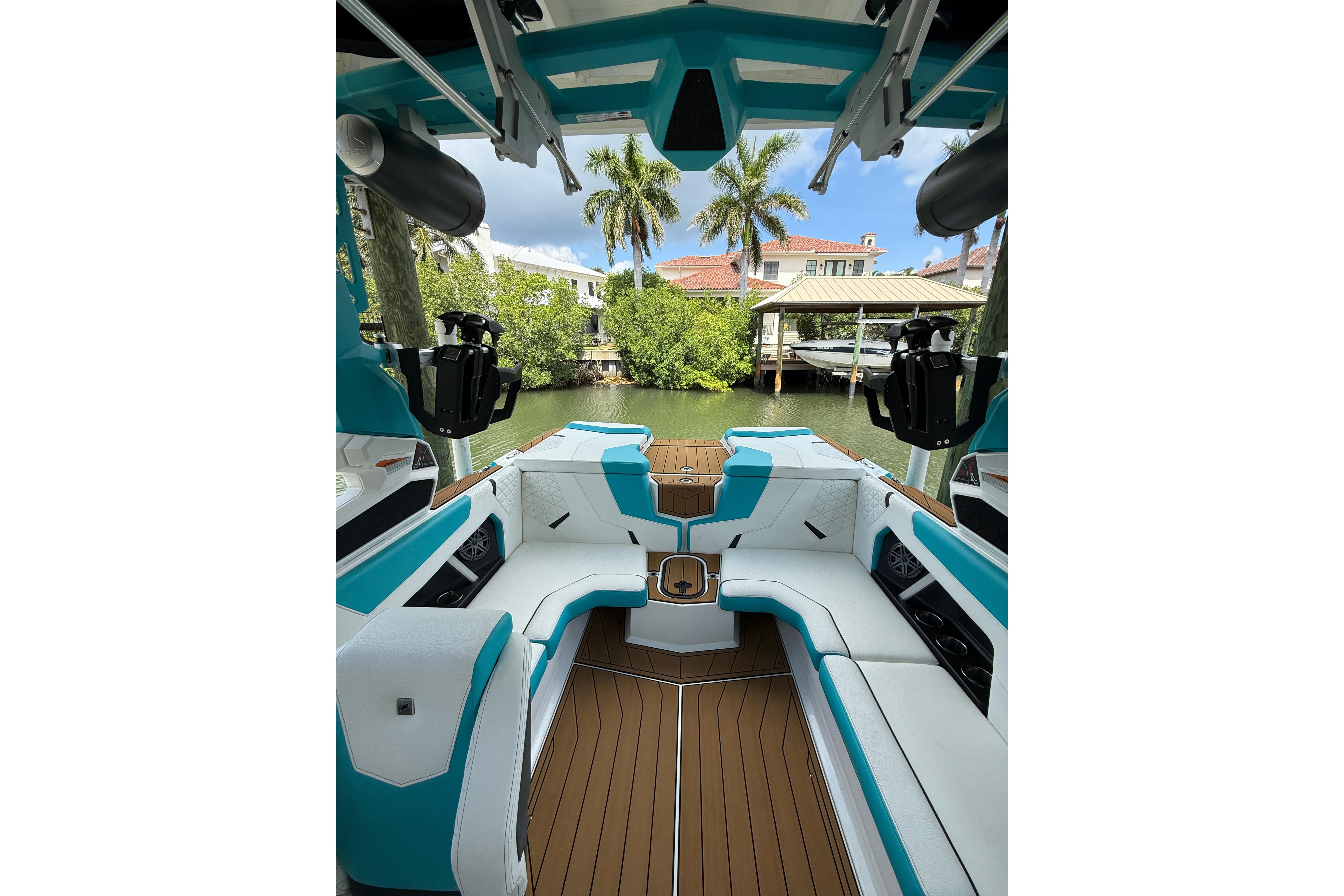 2024 Nautique Super Air Nautique GS20 interior with teal and white seating, docked by lush greenery.