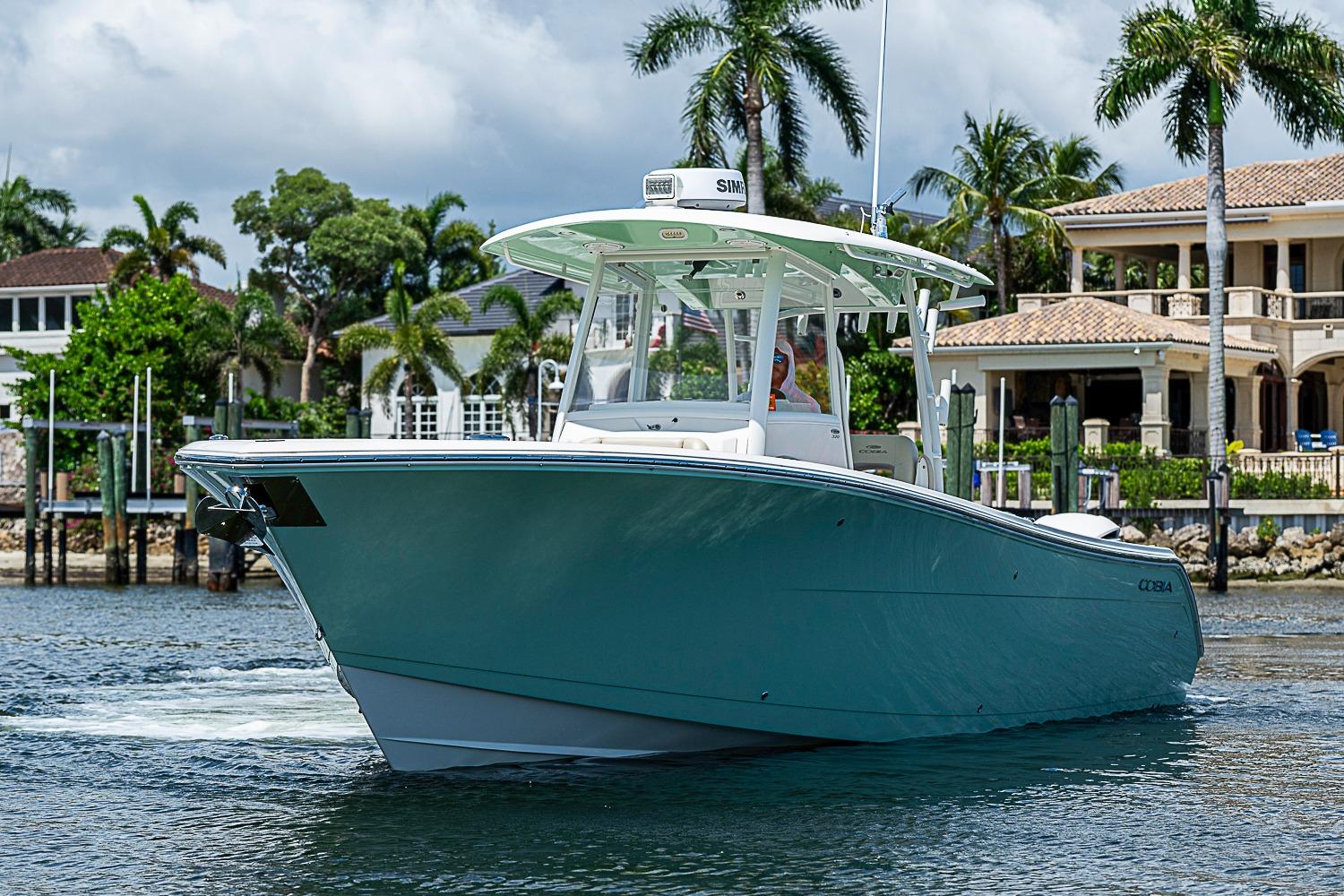 2019 Cobia 320 Center Console boat cruising near waterfront homes and palm trees.