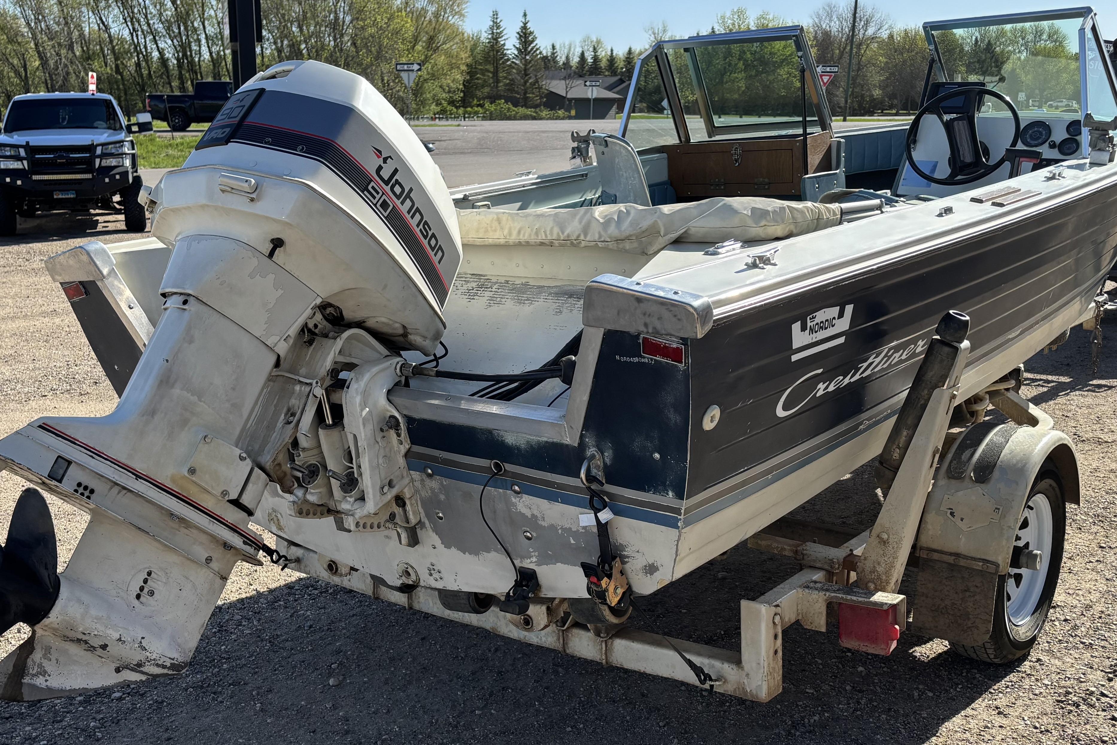 1983 Crestliner 16 boat with Johnson 90 outboard motor on trailer, parked outdoors.