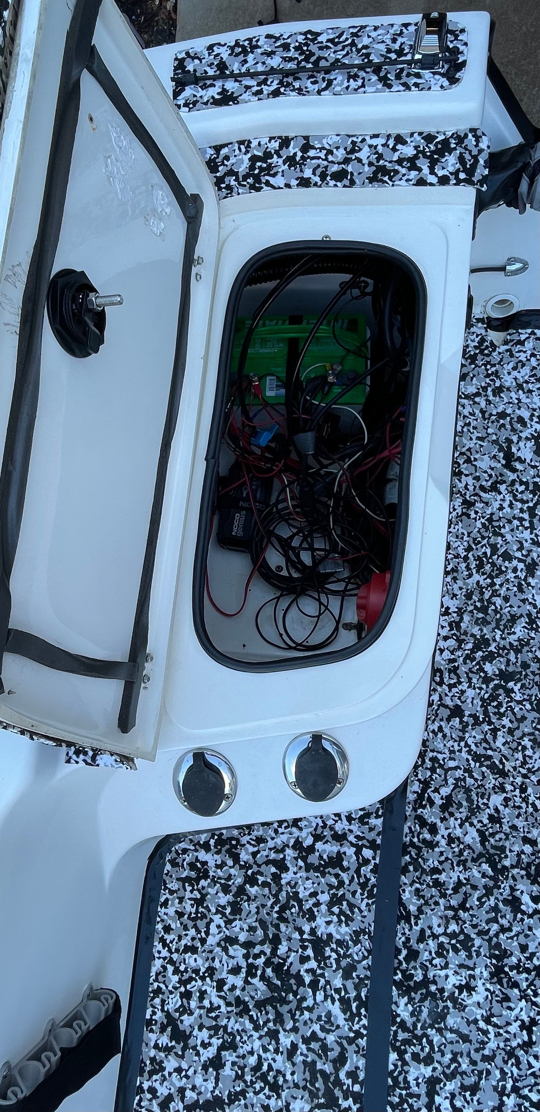 An open storage compartment on a 2006 Mako 2101 Inshore boat reveals cables and electronics.