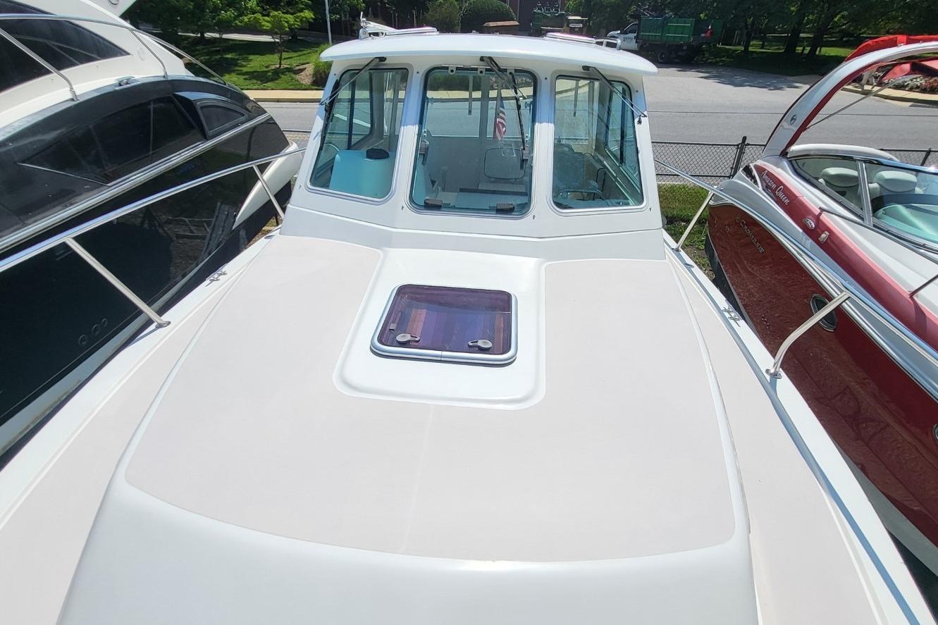 2006 Back Cove 29 boat with sleek white deck and cabin, docked between other boats.
