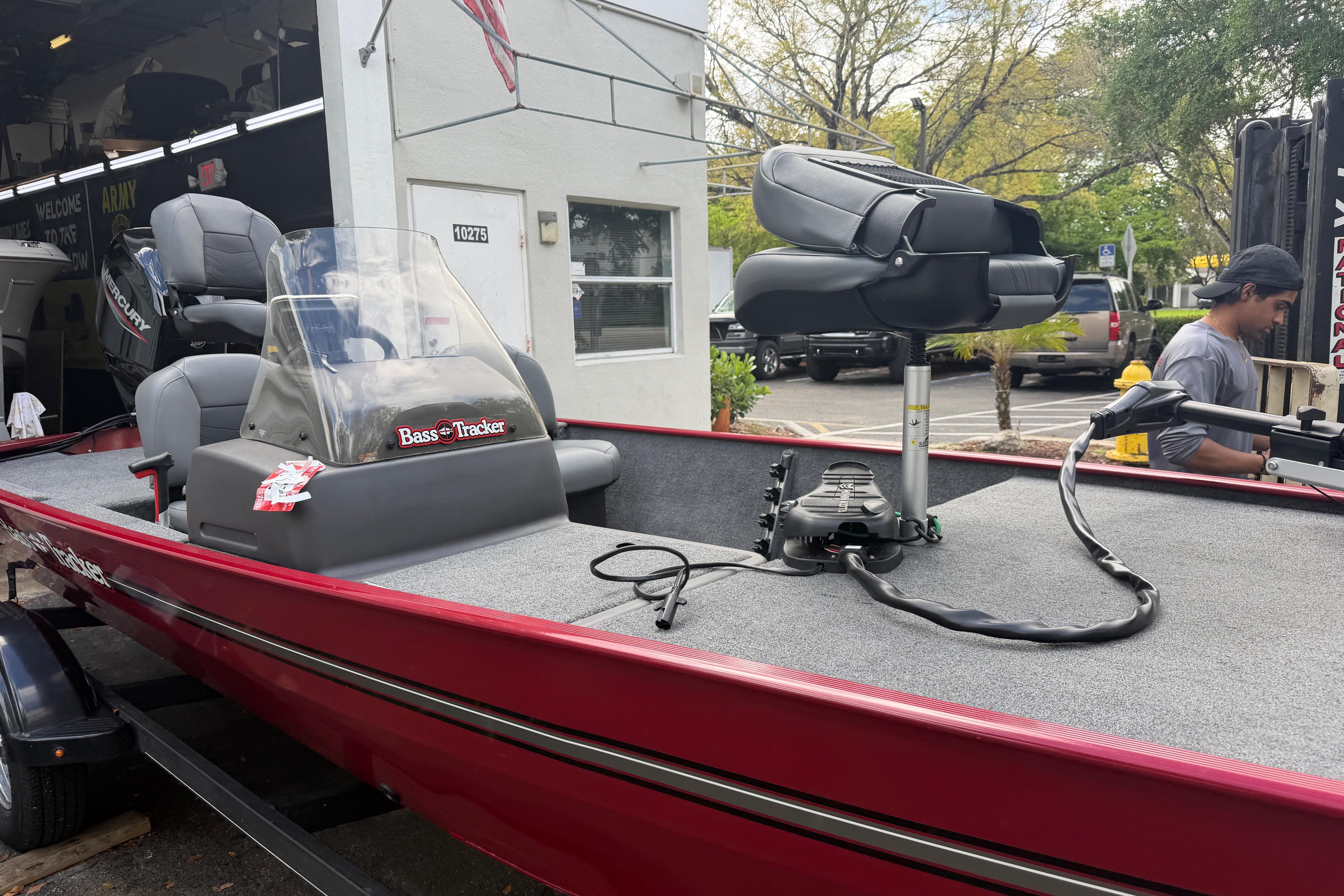 2023 Bass Tracker III Classic boat with red exterior and seating, parked outside a building.