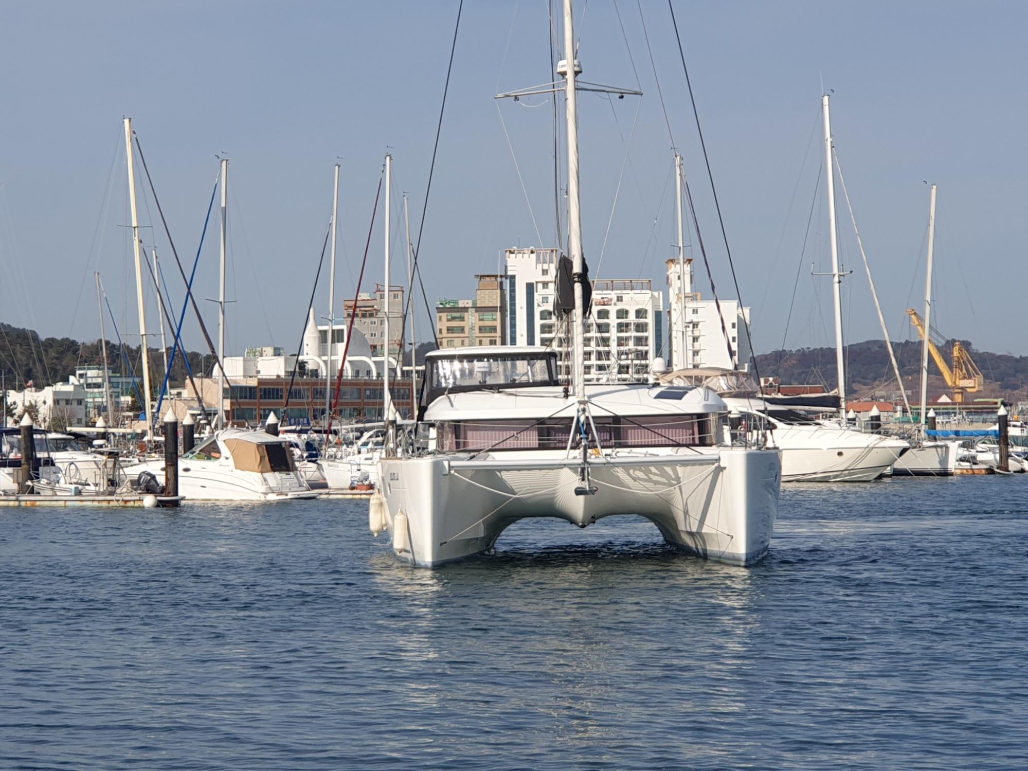 2019 Lagoon 450S catamaran docked in a marina with cityscape background.