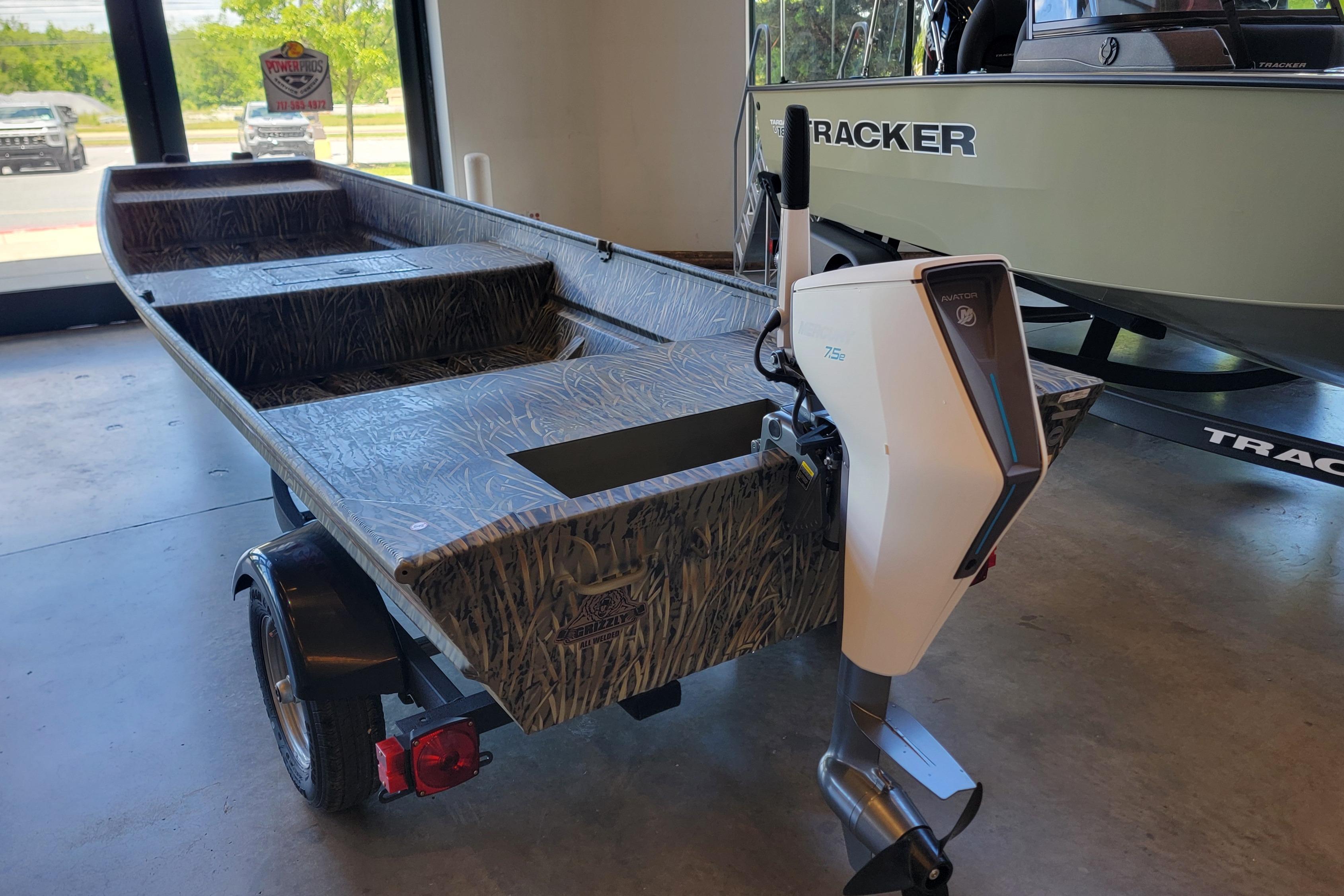 2026 Tracker Grizzly 15 Jon boat with motor, displayed indoors on a trailer.