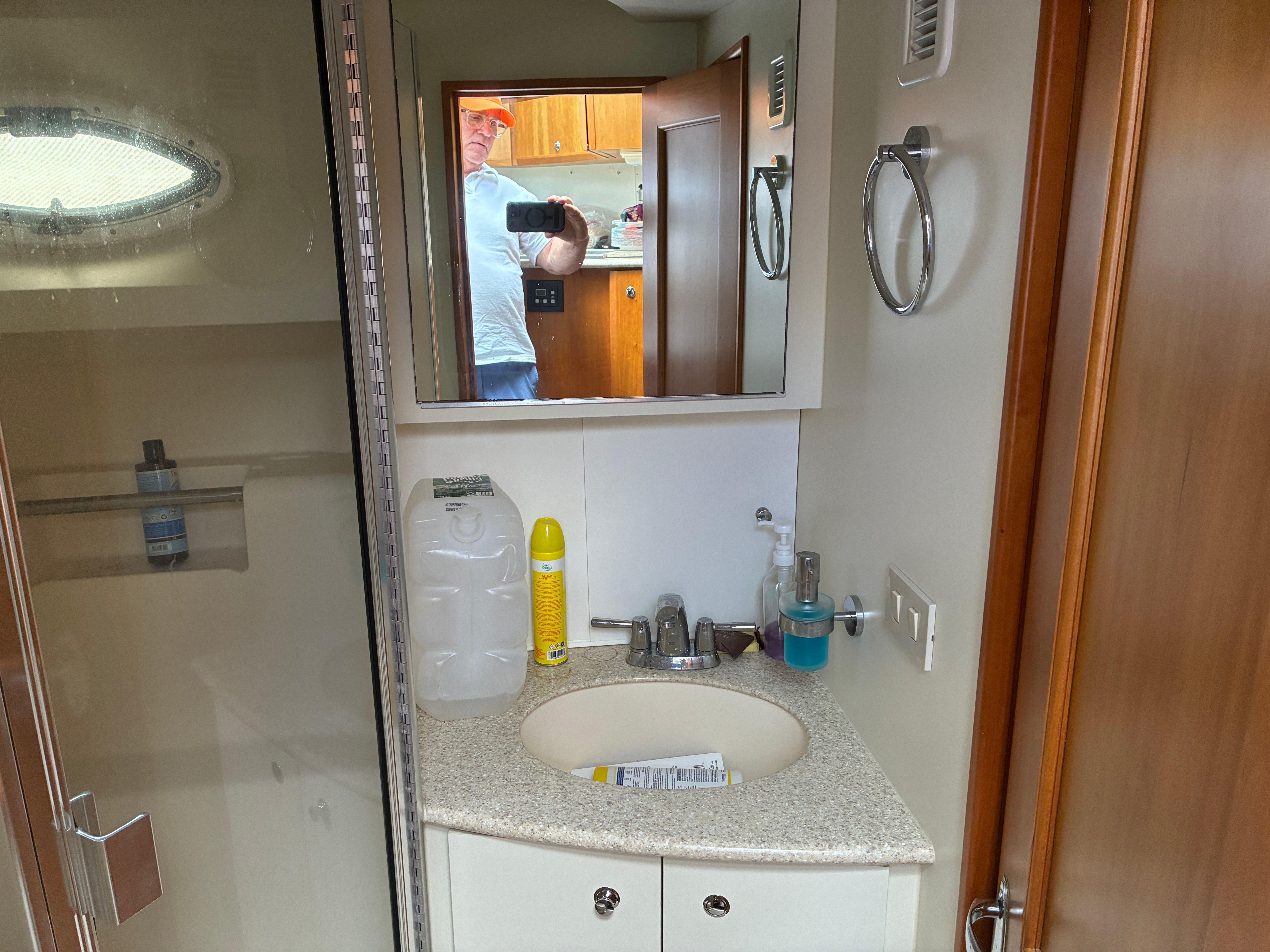 Bathroom in a yacht with sink, mirror, and shower. A person is visible in the mirror.